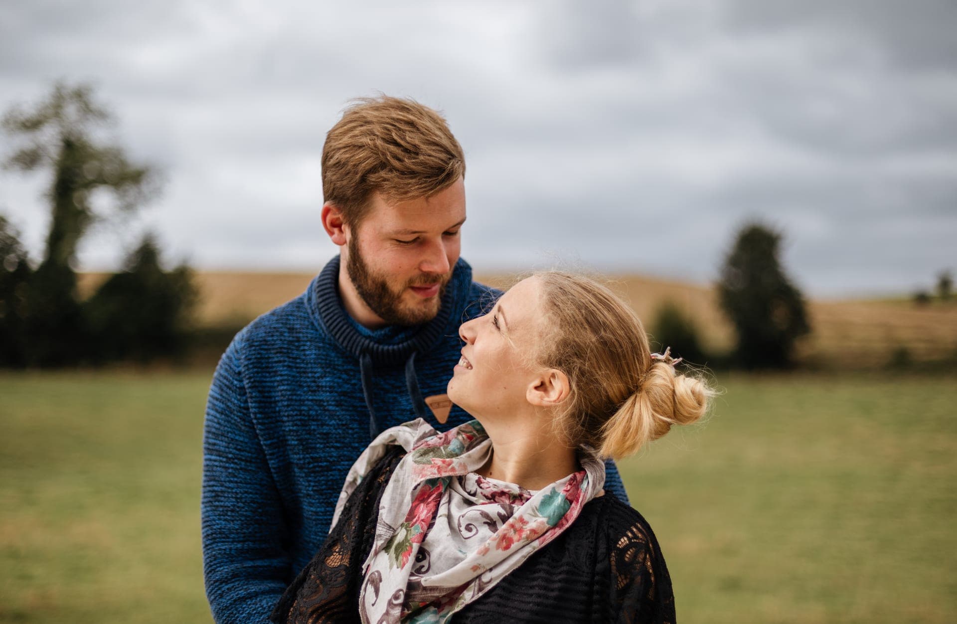 Couple regard tendre face à face dans un champ pull bleu marine ciel d'automne — séance couple nature Aurore Clercq Photographie Belgique