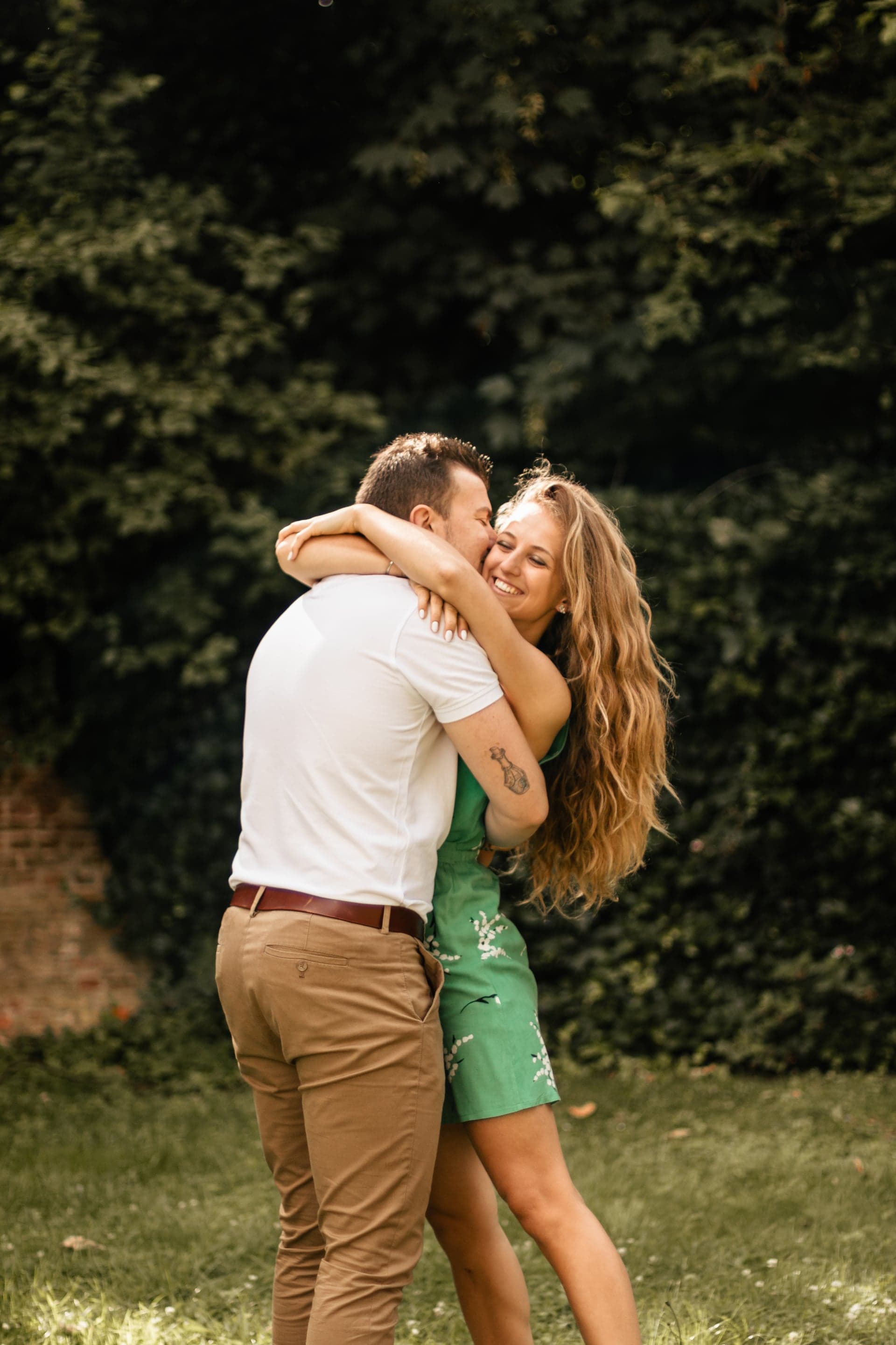 Couple enlacé dans le jardin robe verte éclat de rire — séance couple joyeuse été