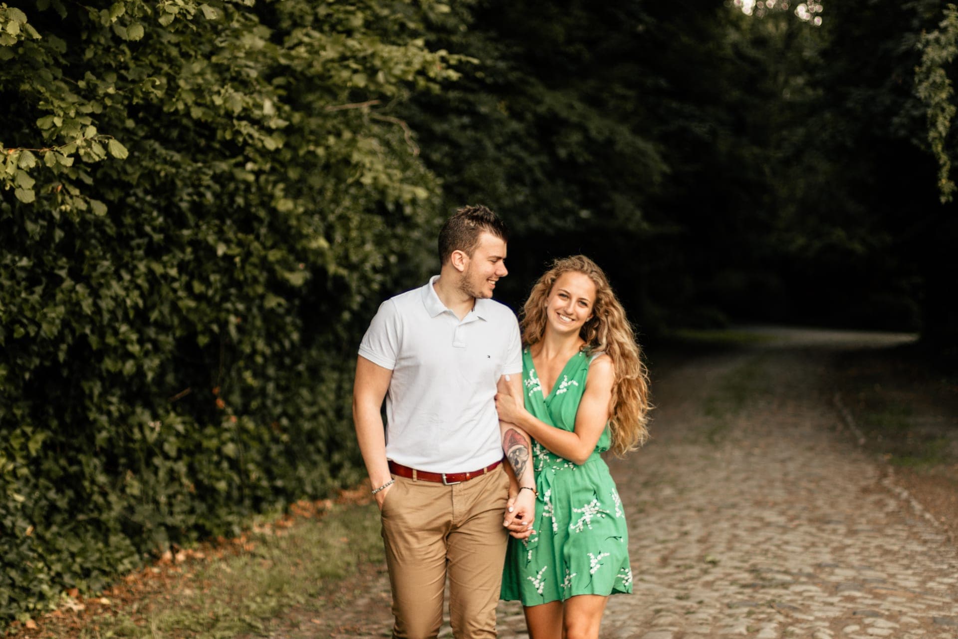 Couple qui marche main dans la main sur un chemin pavé en forêt — séance couple Brabant Wallon