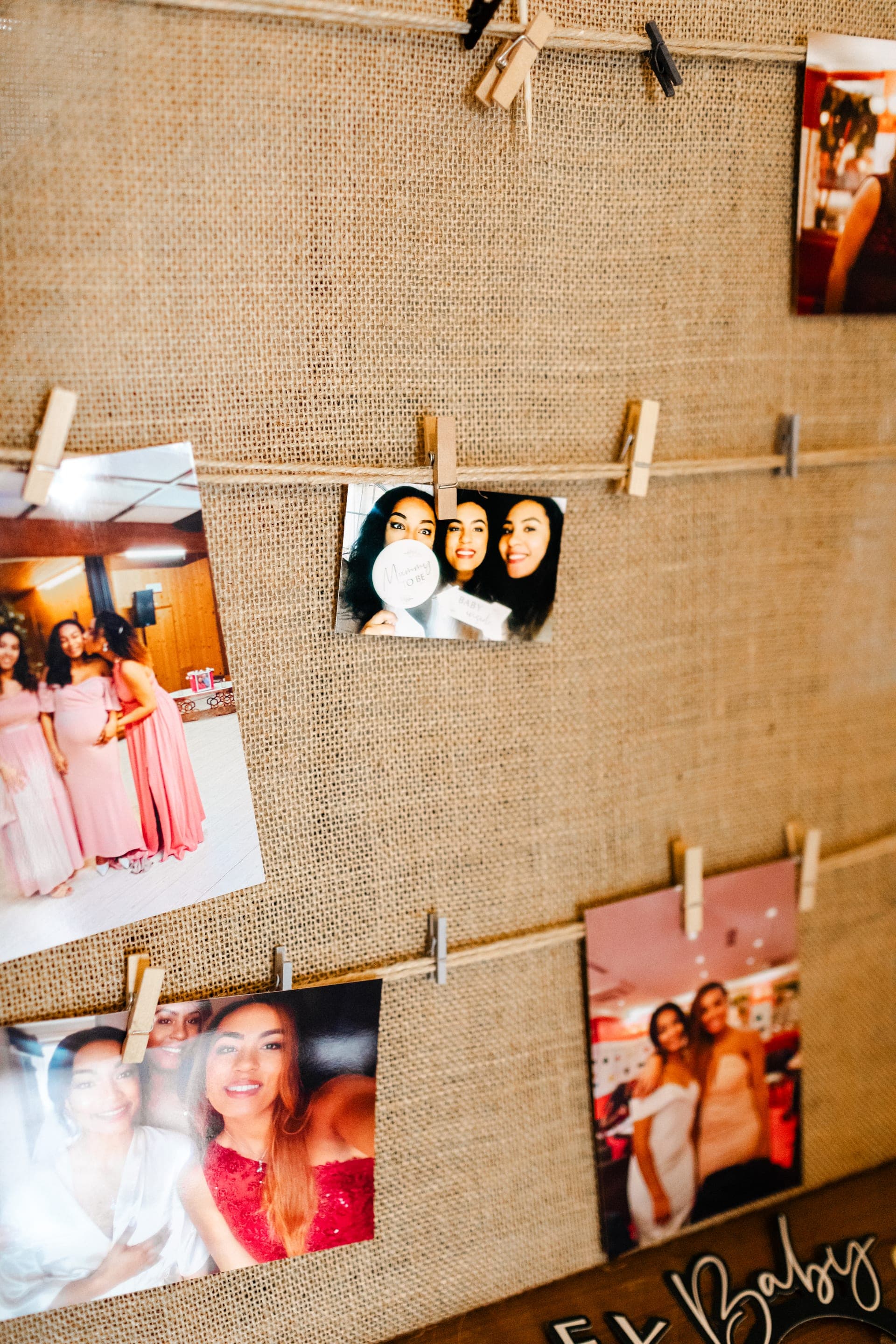 Détail mur de souvenirs photos pendues à des cordes sur fond de jute By Baby — reportage baby shower décor