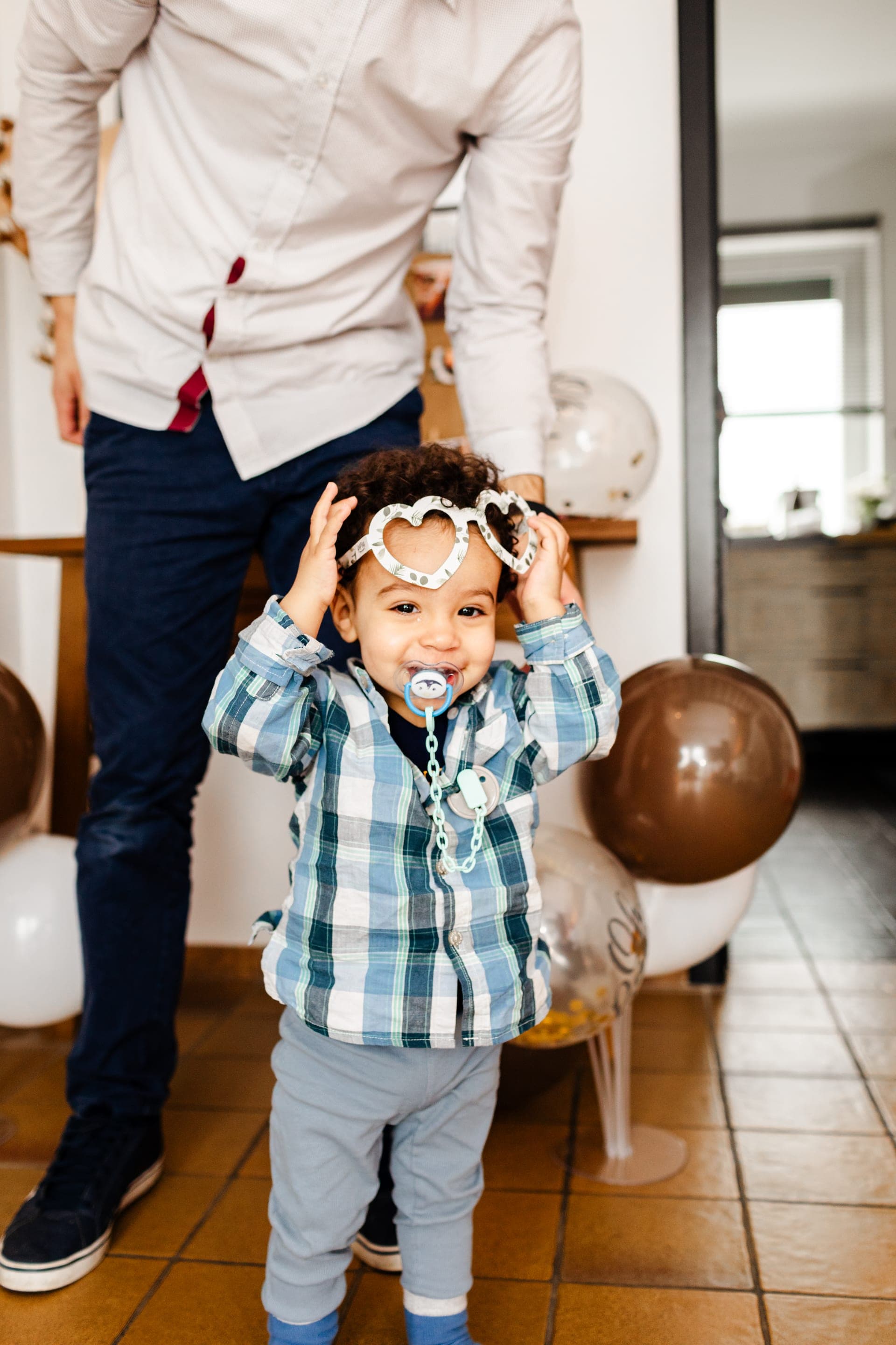 Petit garçon en chemise carreaux avec lunettes en cœur sur le front papa en arrière-plan — reportage baby shower candid