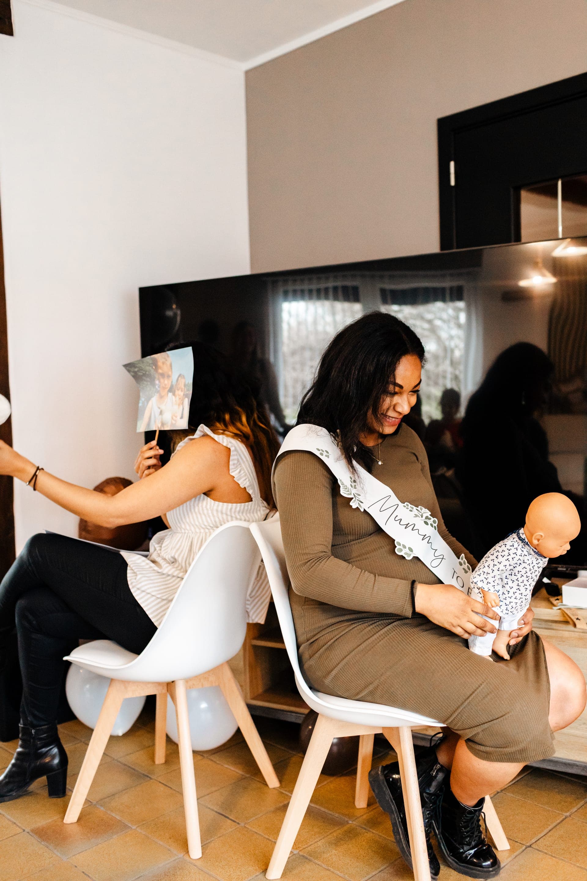 Future maman avec poupon et amie tenant une photo moment spontané du jeu Mummy to Be — reportage baby shower convivial