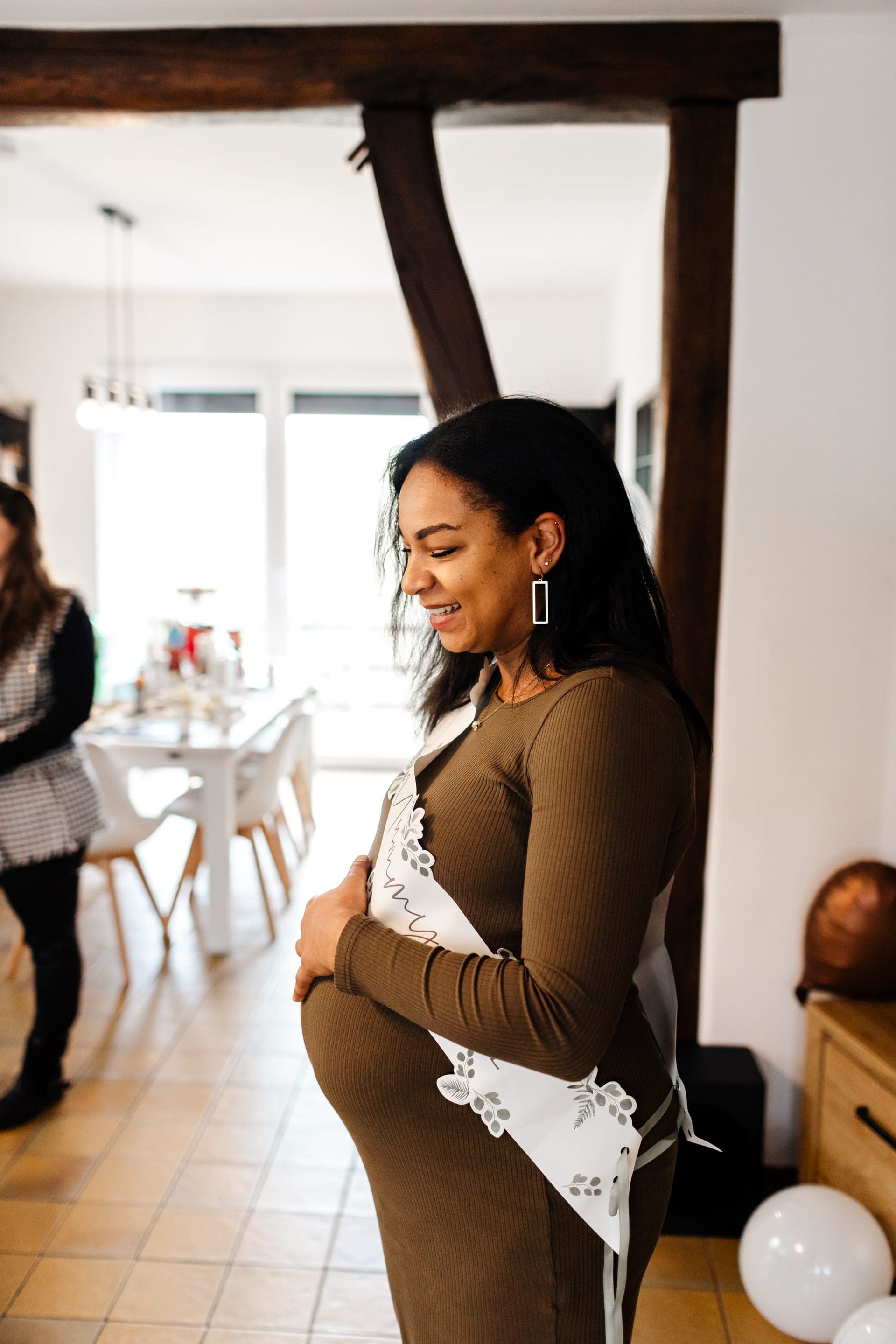 Future maman de profil mains posées sur son ventre sourire tendre — reportage baby shower intimiste à domicile