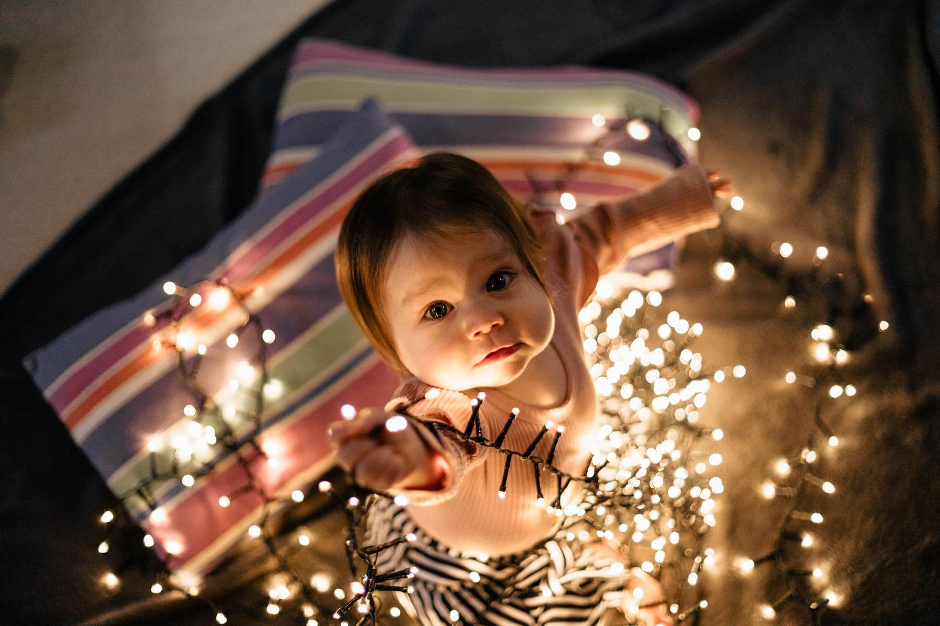 Bébé joue avec une guirlande lumineuse magie de Noël — séance famille Noël