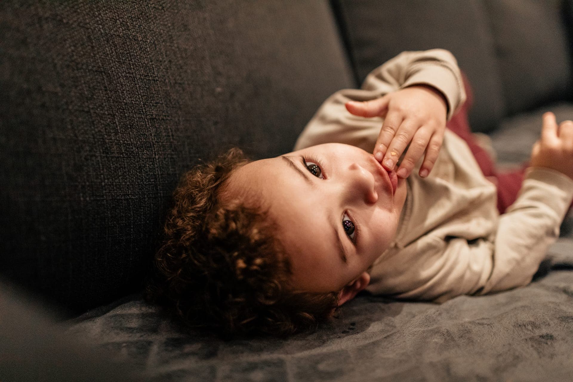 Enfant allongé sur le canapé regard caméra intime — séance famille lifestyle maison
