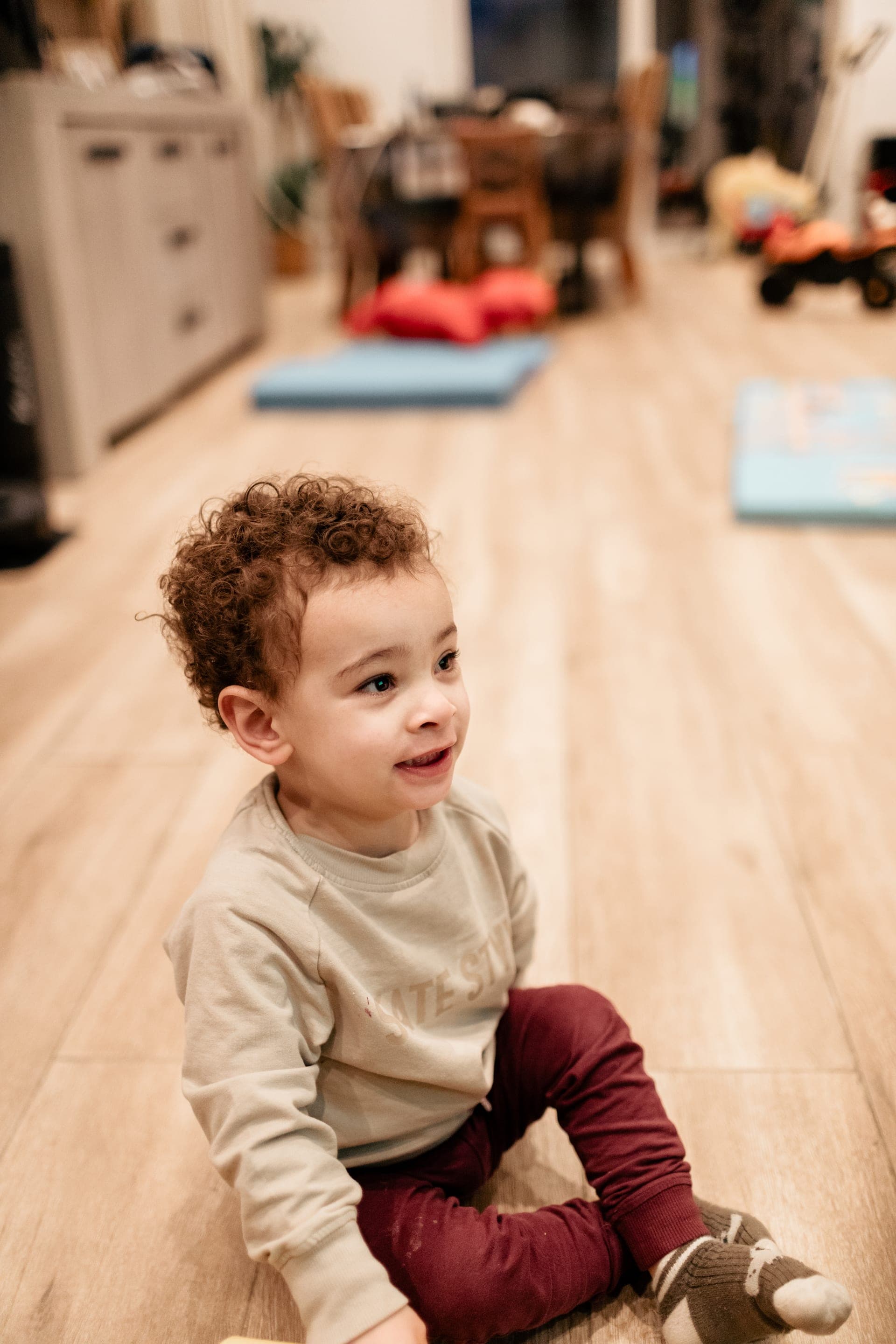 Enfant assis au sol du salon sourire — séance famille lifestyle maison