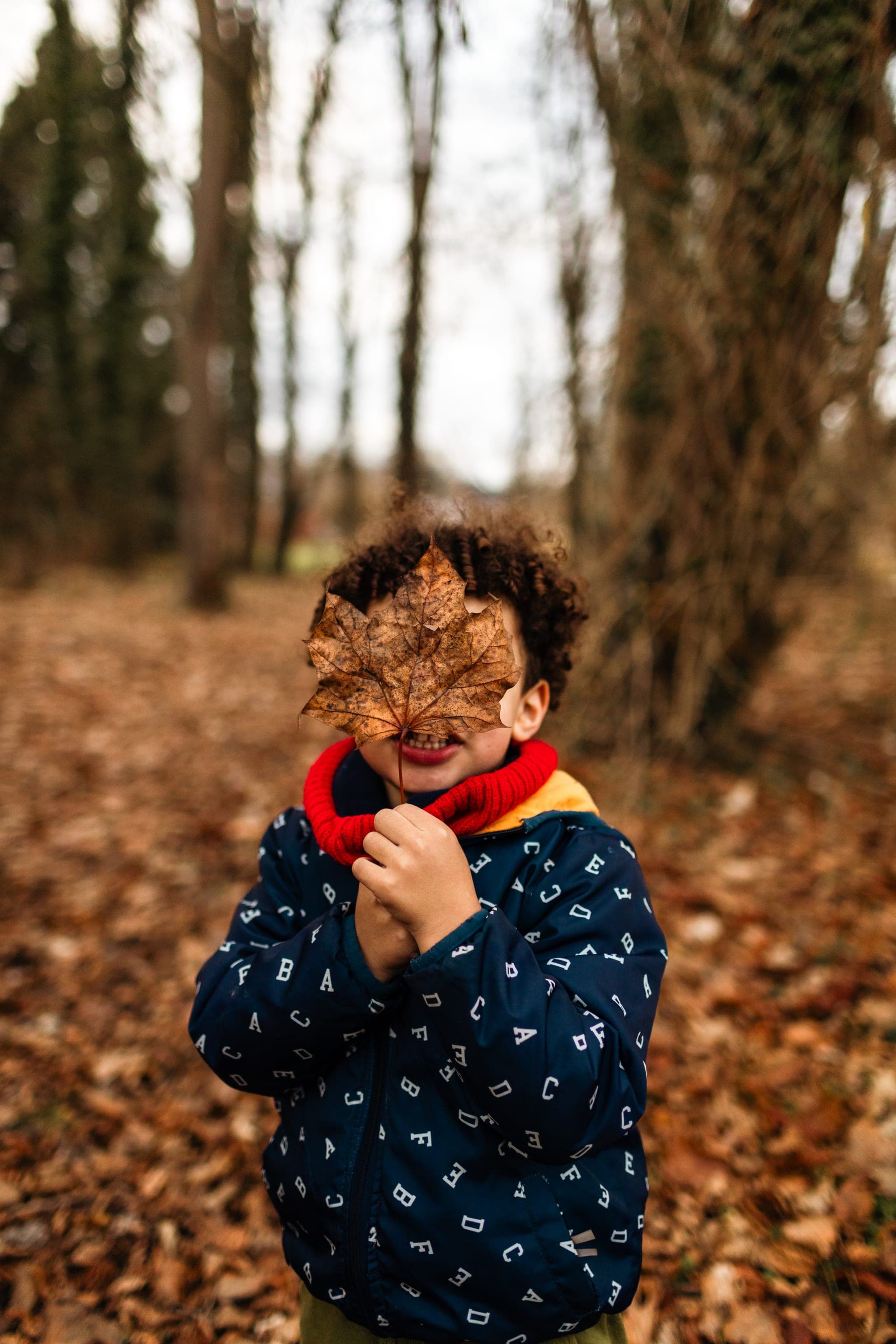 Enfant cache son visage derrière une feuille morte en automne — séance famille jeu parc