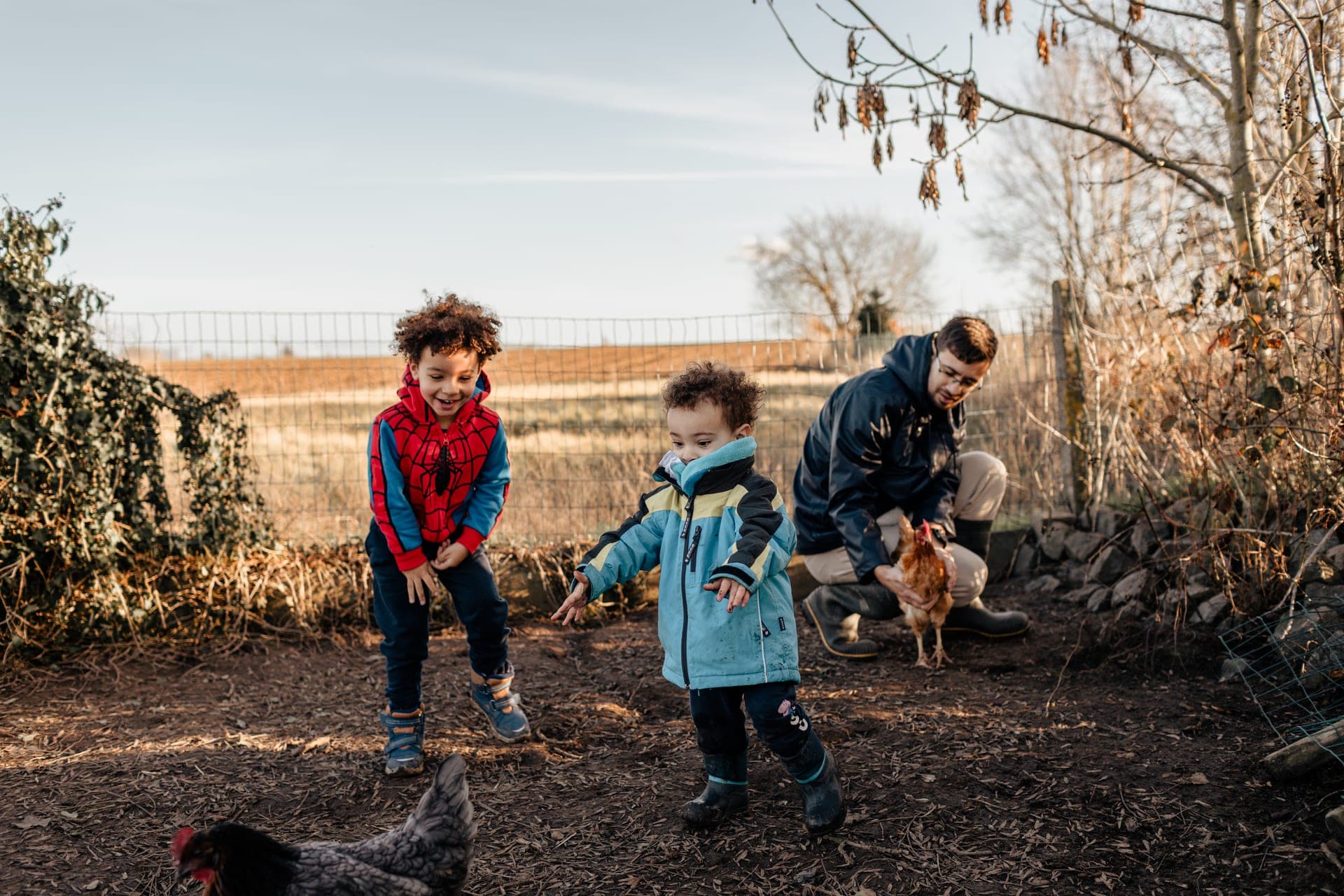 Enfants et papa avec des poules dans la cour d'une ferme à la campagne — séance famille lifestyle