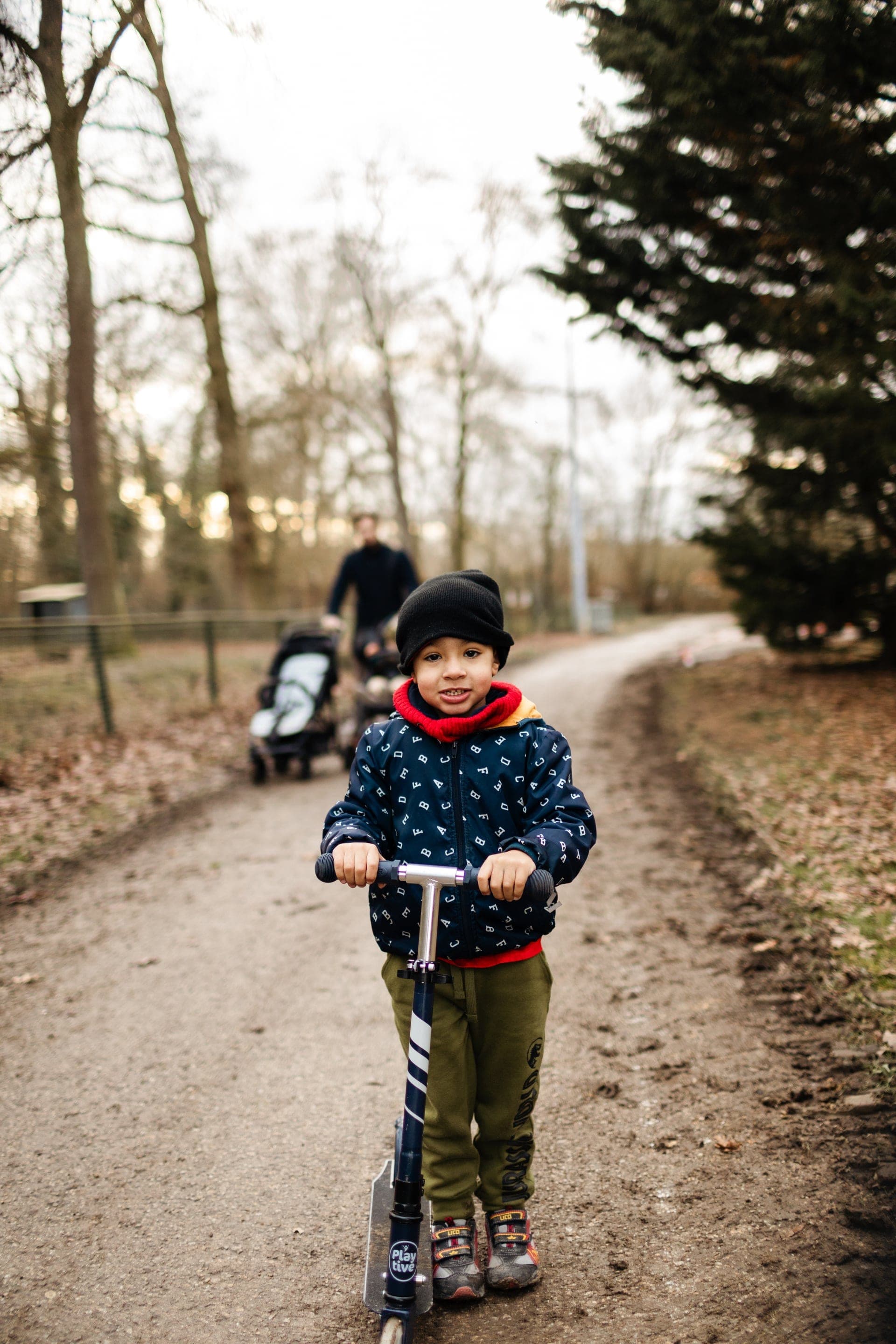 Garçon bonnet noir sur trottinette chemin de parc en hiver — séance famille extérieur