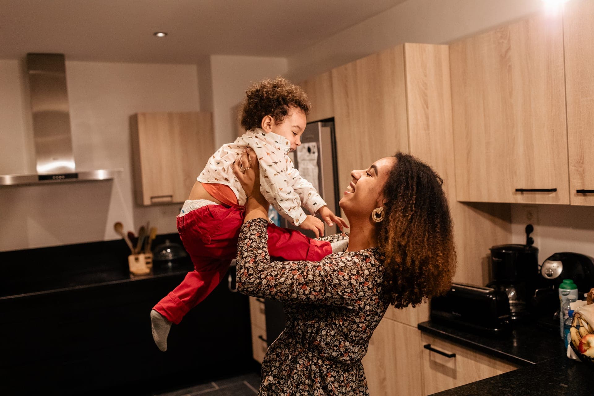 Maman soulève son enfant en l'air dans la cuisine fou rire — séance famille complicité