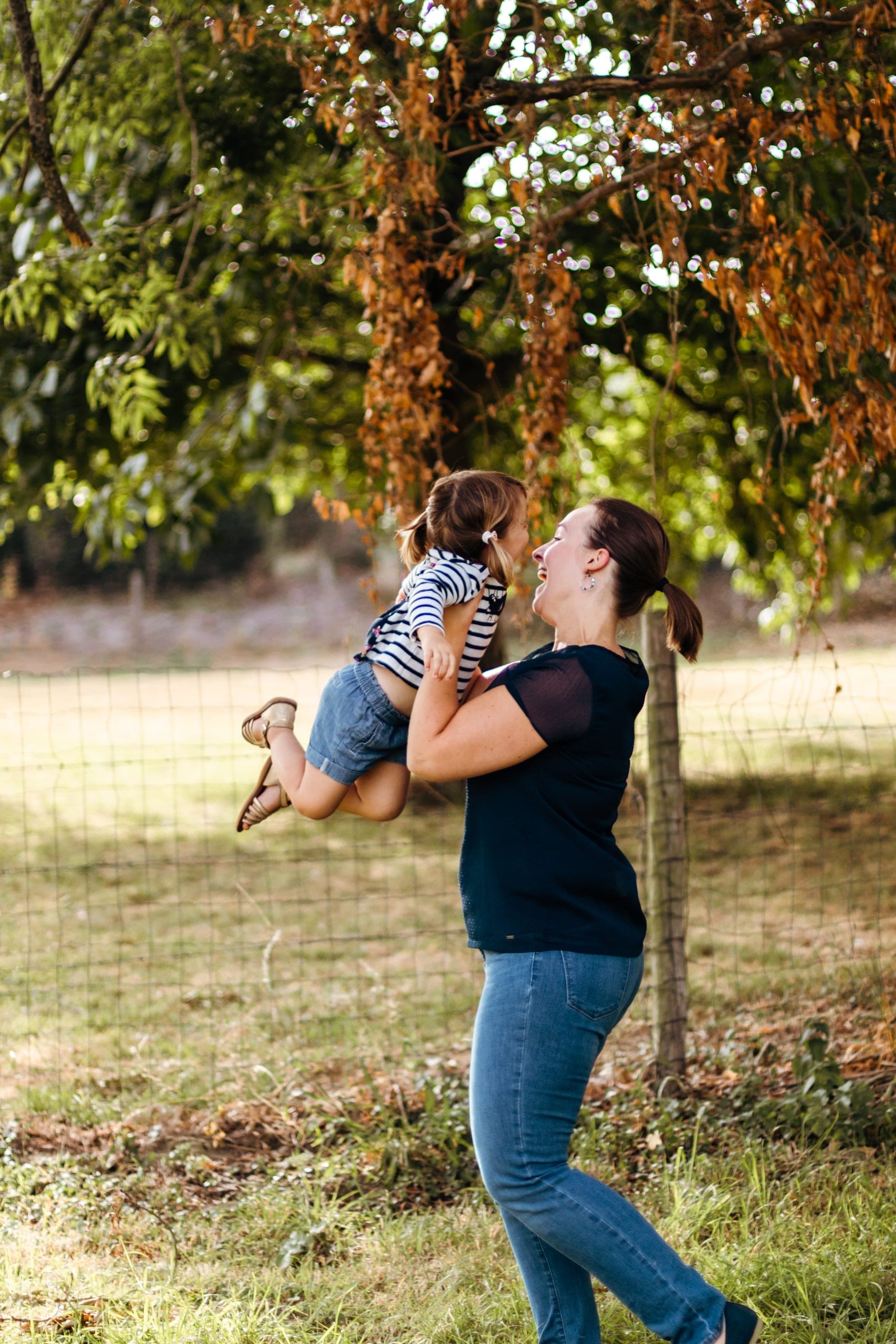 Maman soulève sa fille nez à nez dans le jardin en automne — séance famille joyeuse