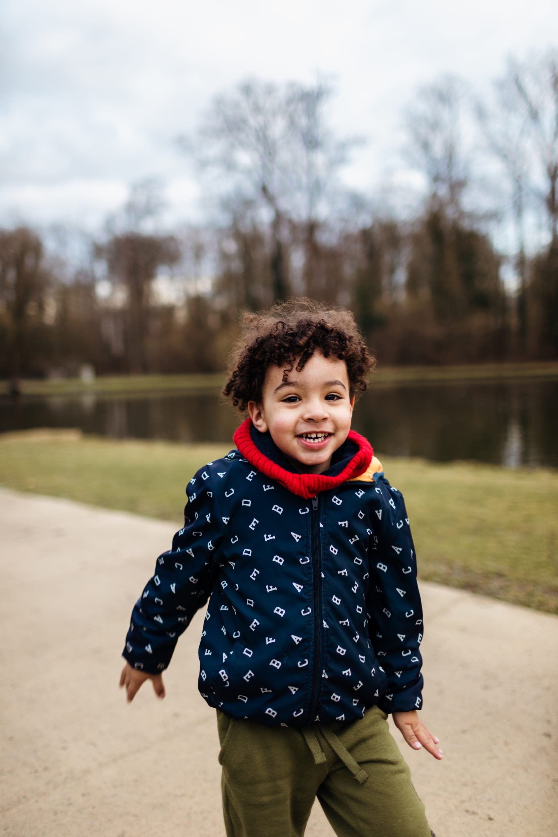Portrait enfant bonnet noir écharpe rouge sourire radieux au parc — séance famille hiver