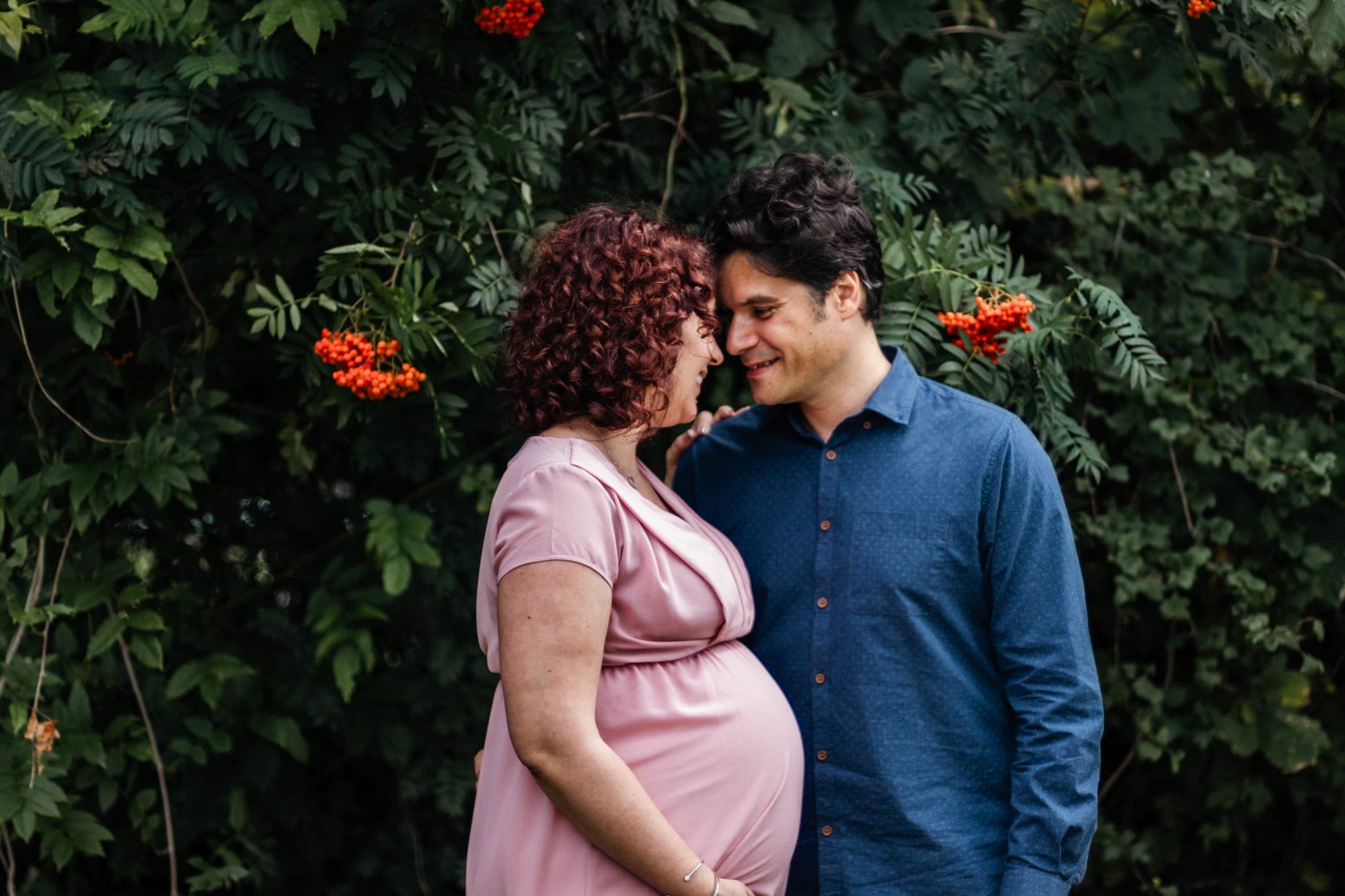 Couple enceinte sous un arbuste aux fleurs oranges — séance grossesse poétique