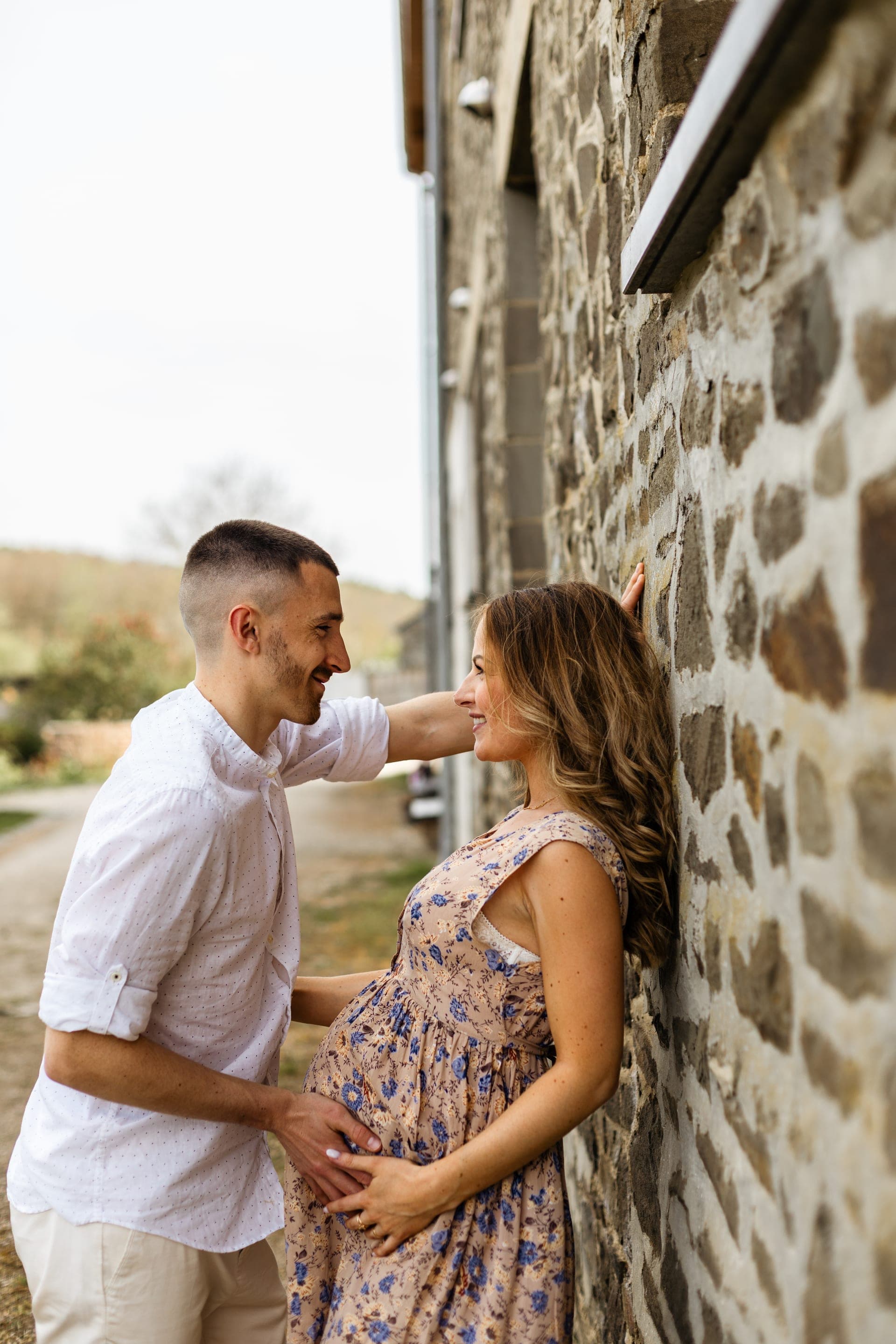 Couple enceinte contre un mur de pierre robe fleurie — séance grossesse champêtre