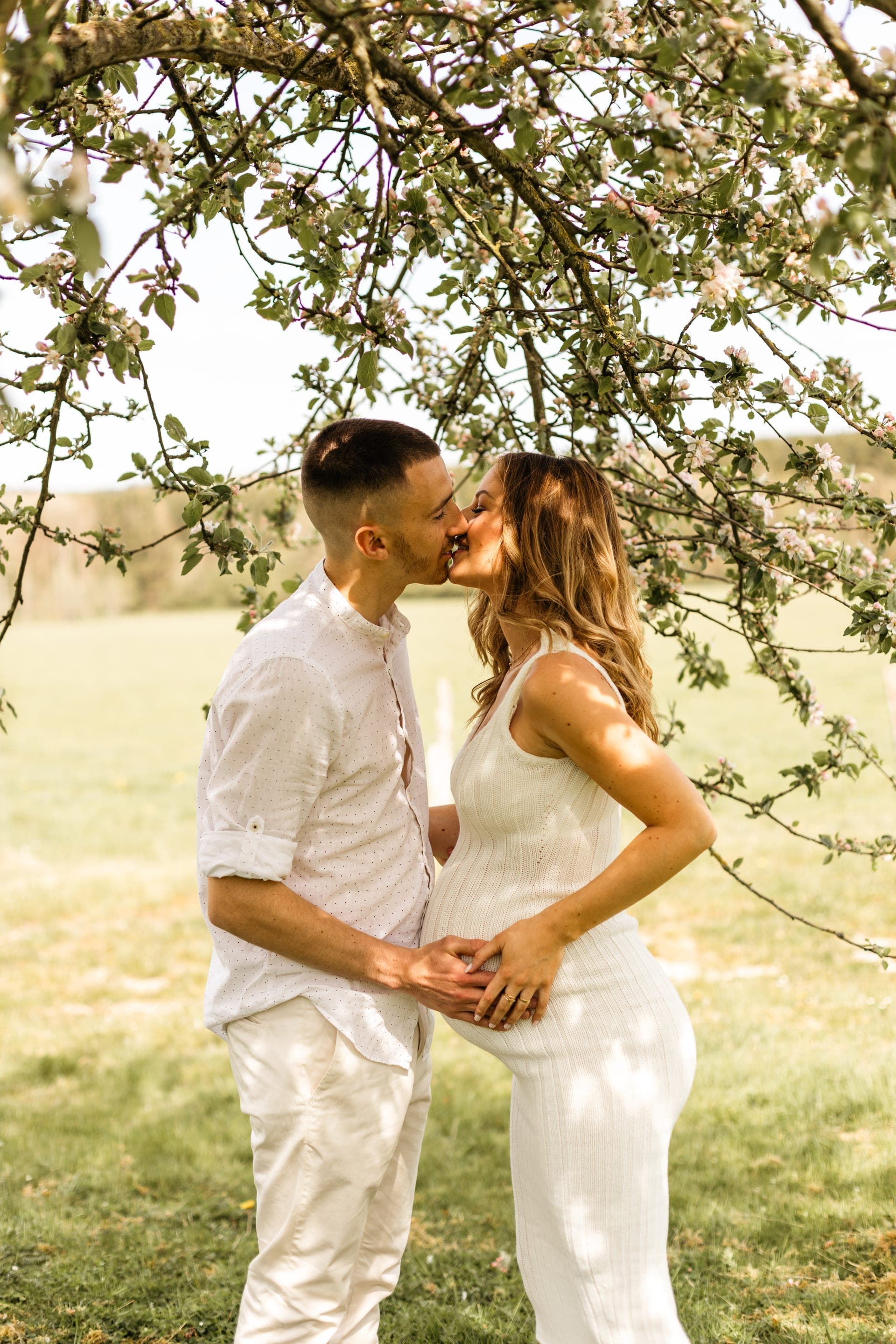 Couple enceinte baiser sous pommier en fleurs au printemps — séance grossesse tendresse