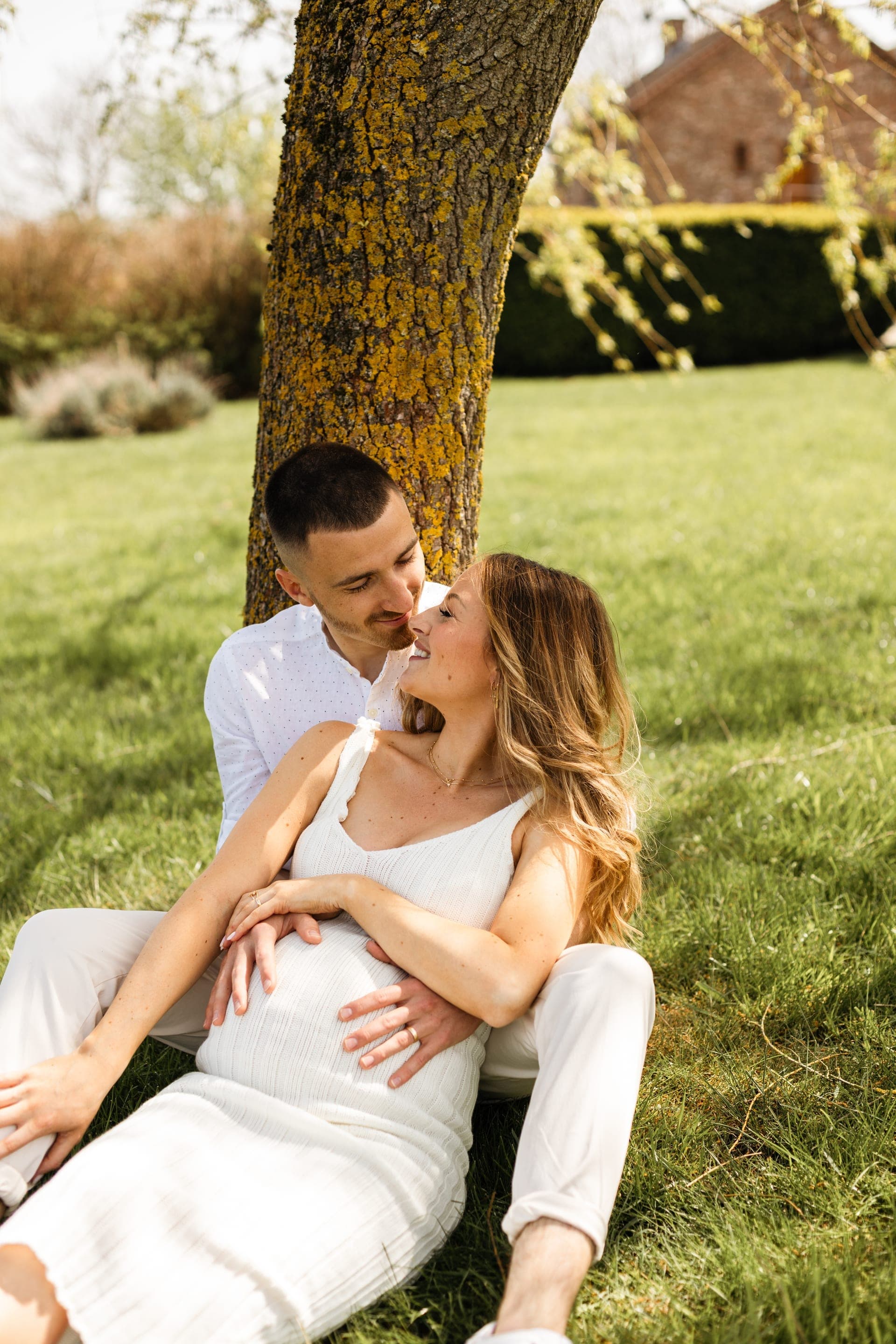 Couple enceinte assis sous un arbre au printemps complicité — grossesse extérieur nature
