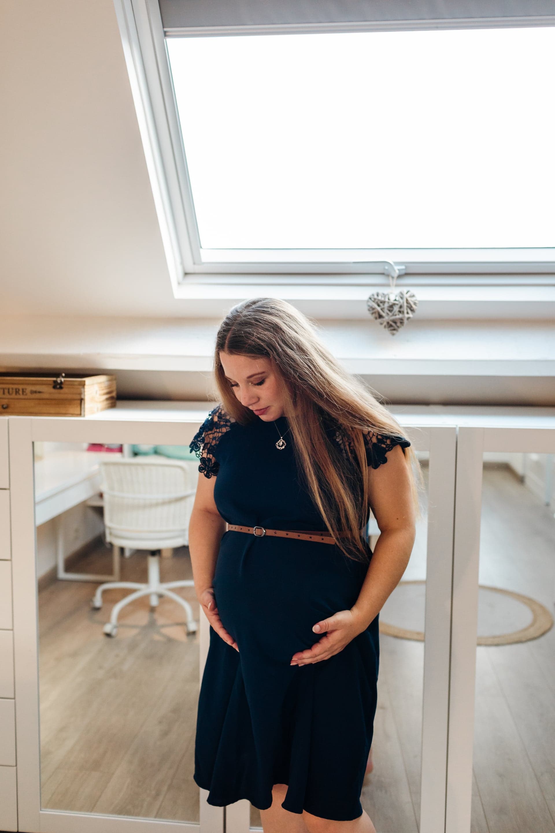 Future maman debout dans la chambre bébé robe bleu marine regard vers le ventre — séance grossesse préparatifs