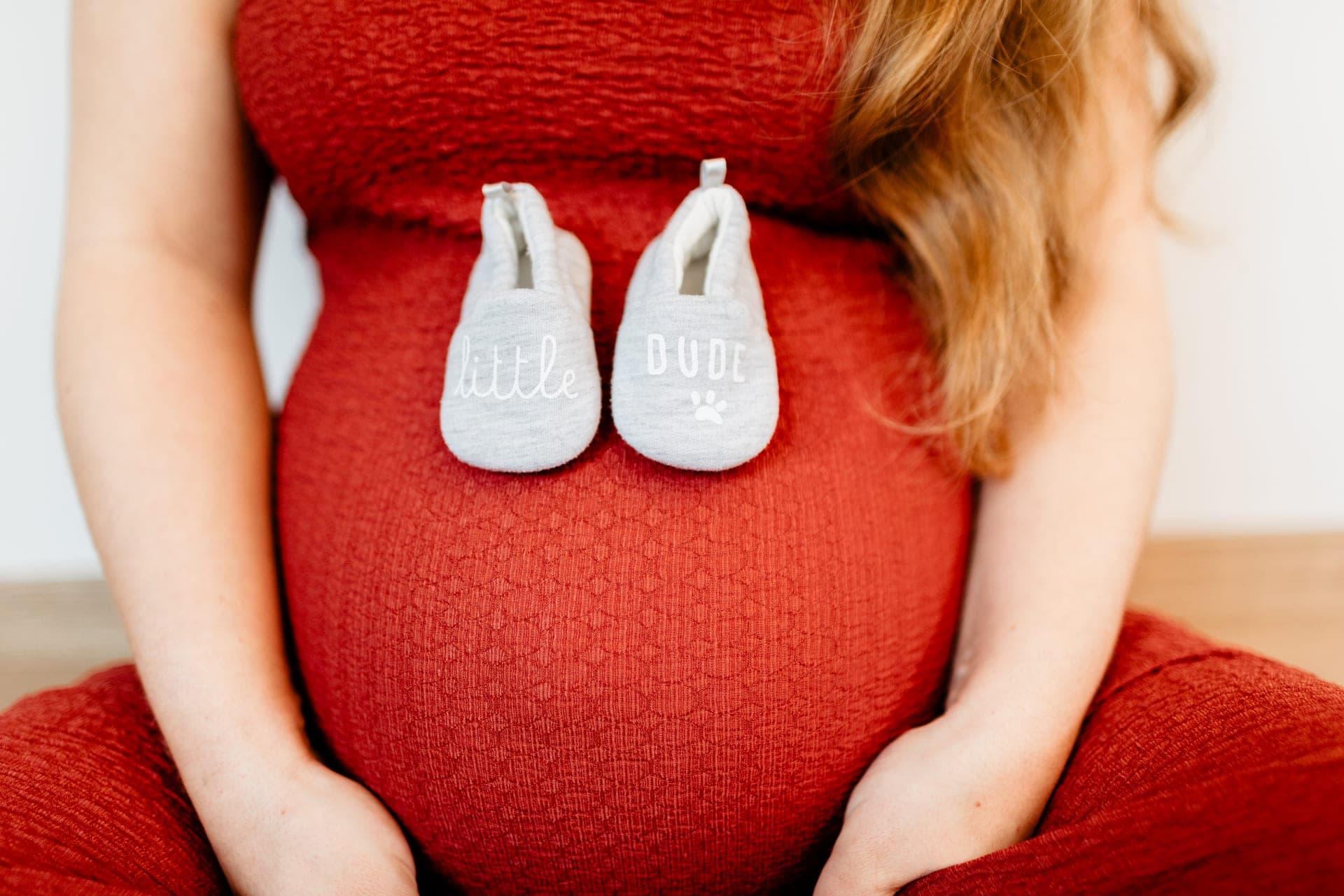 Petits chaussons Little Dude posés sur le ventre de grossesse rouge — détail grossesse