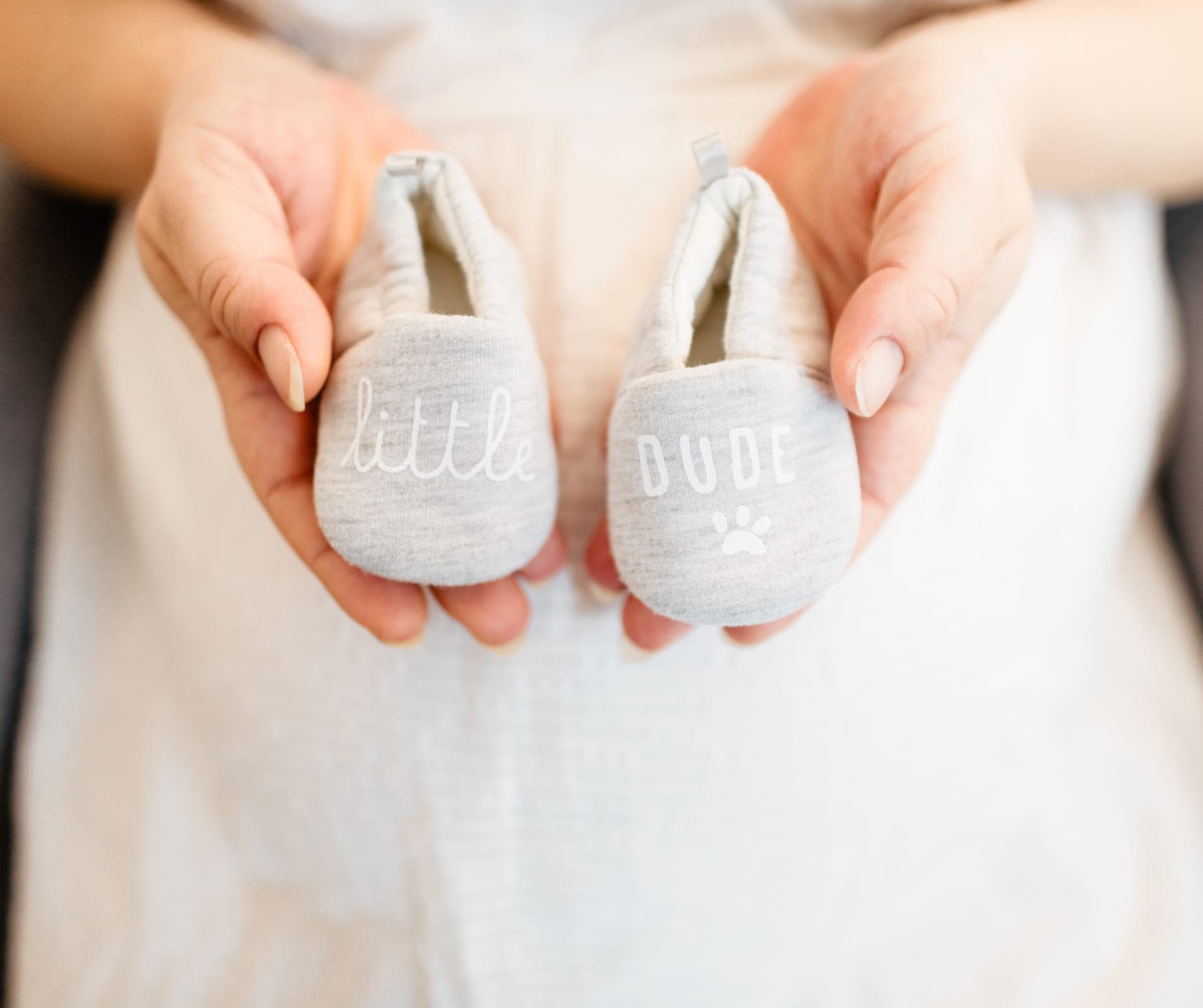 Chaussons de bébé tenus dans les mains de la future maman — détail préparatifs grossesse