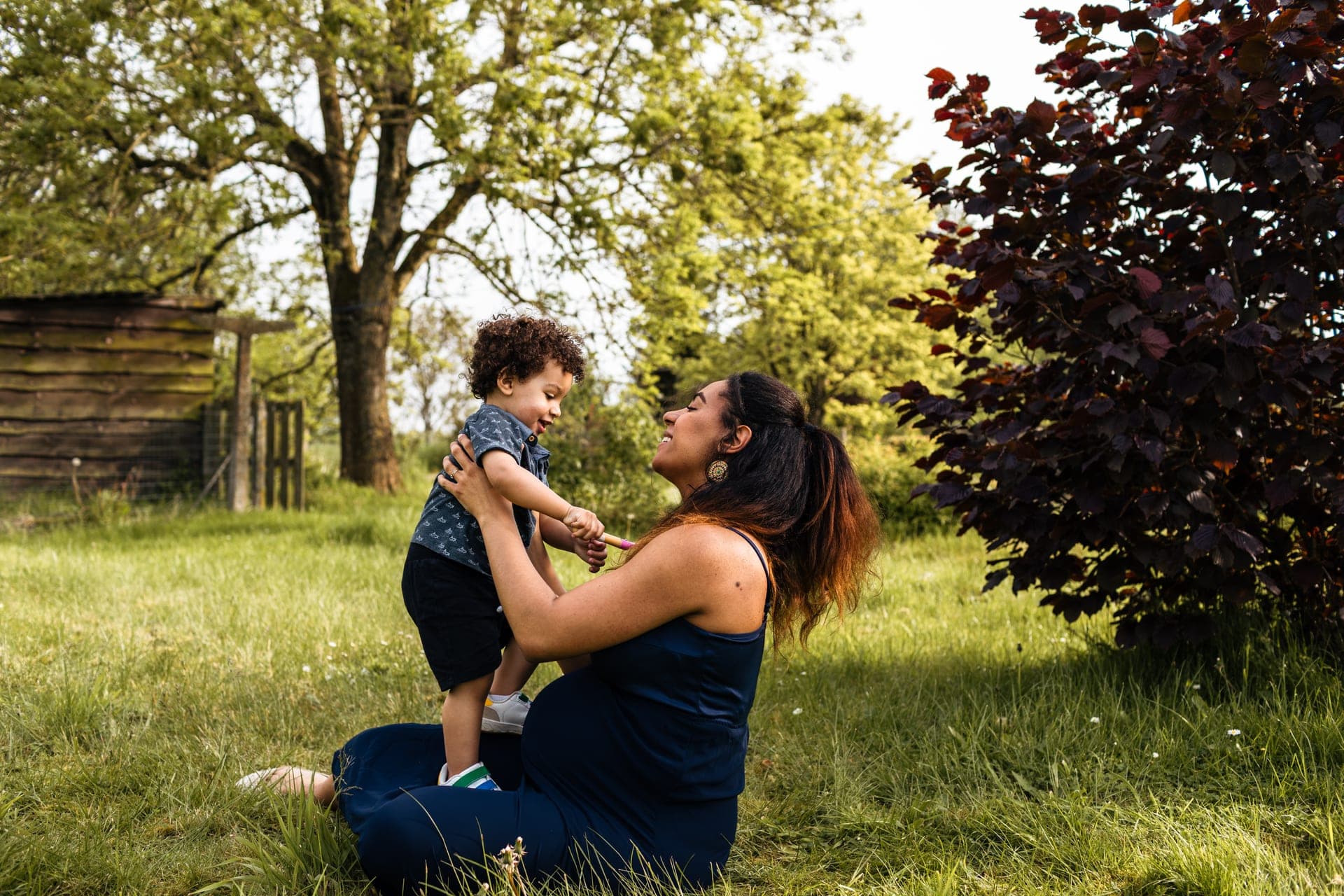 Enfant debout sur les genoux de sa maman enceinte — séance grossesse famille complicité