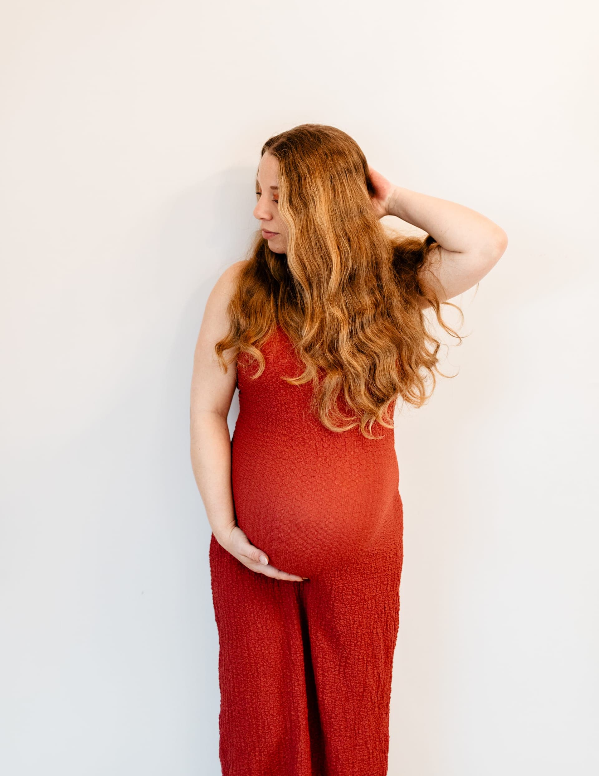 Femme enceinte debout en robe rouge terracotta en studio — force et beauté