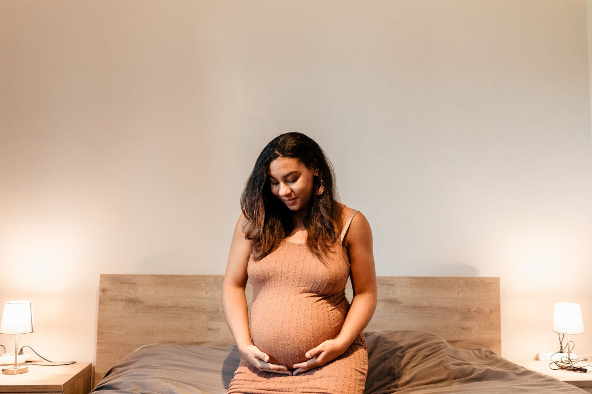 Future maman assise sur son lit entre les lampes de chevet — lifestyle grossesse