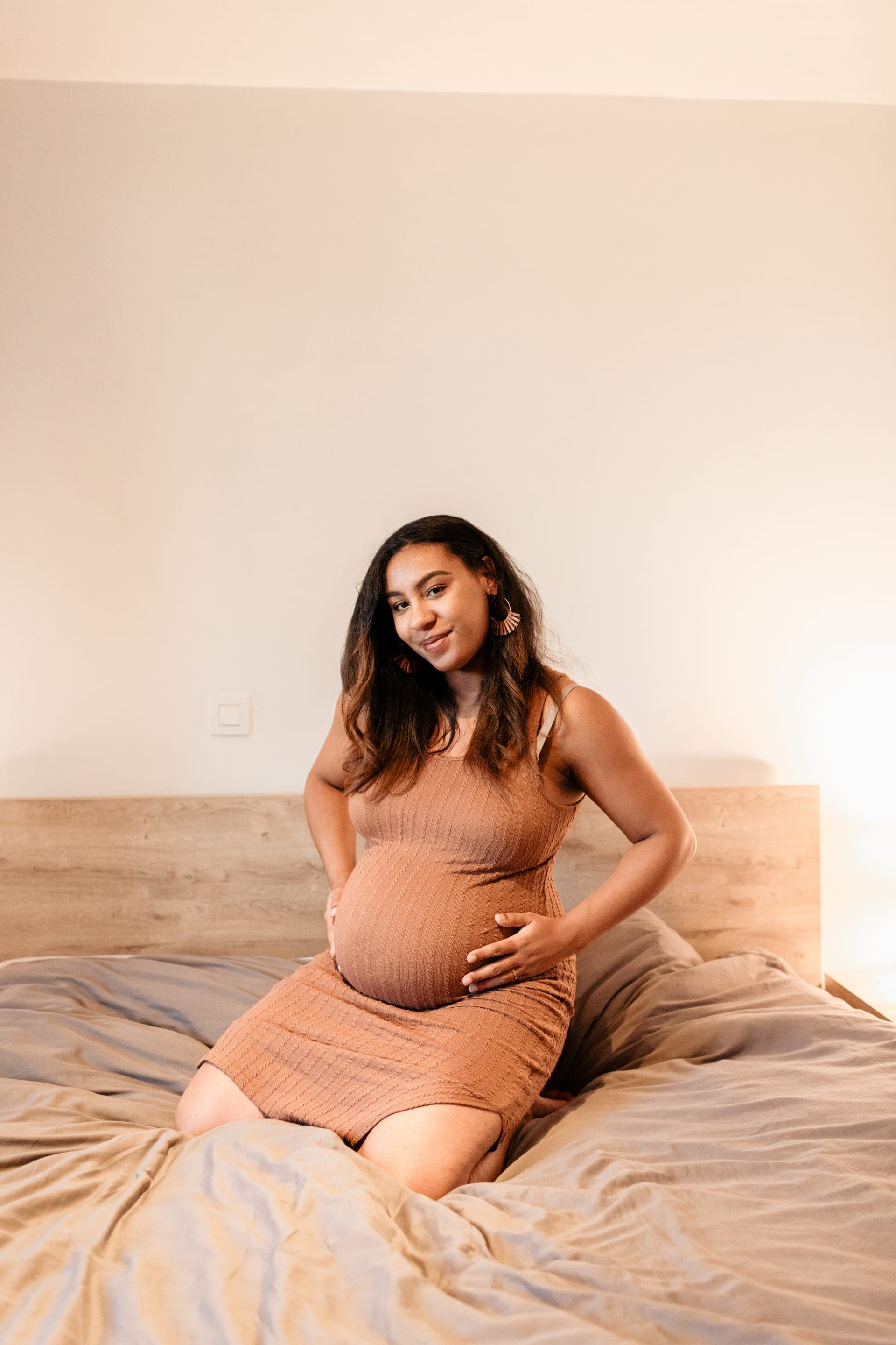 Portrait femme enceinte sur son lit robe caramel regard caméra — séance grossesse intime