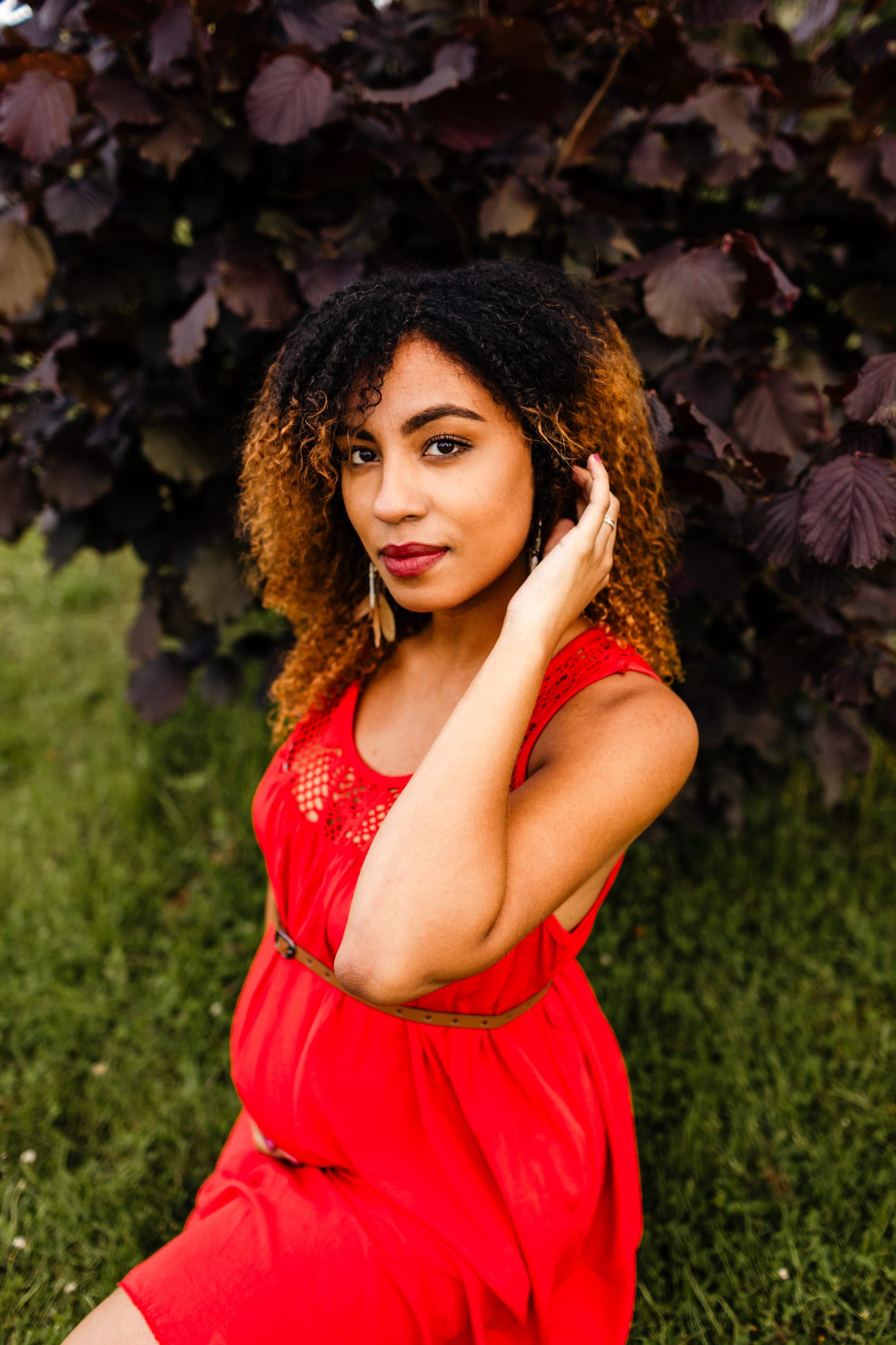 Portrait femme enceinte robe rouge cheveux bouclés devant feuillage pourpre — séance grossesse Aurore Clercq Photographie