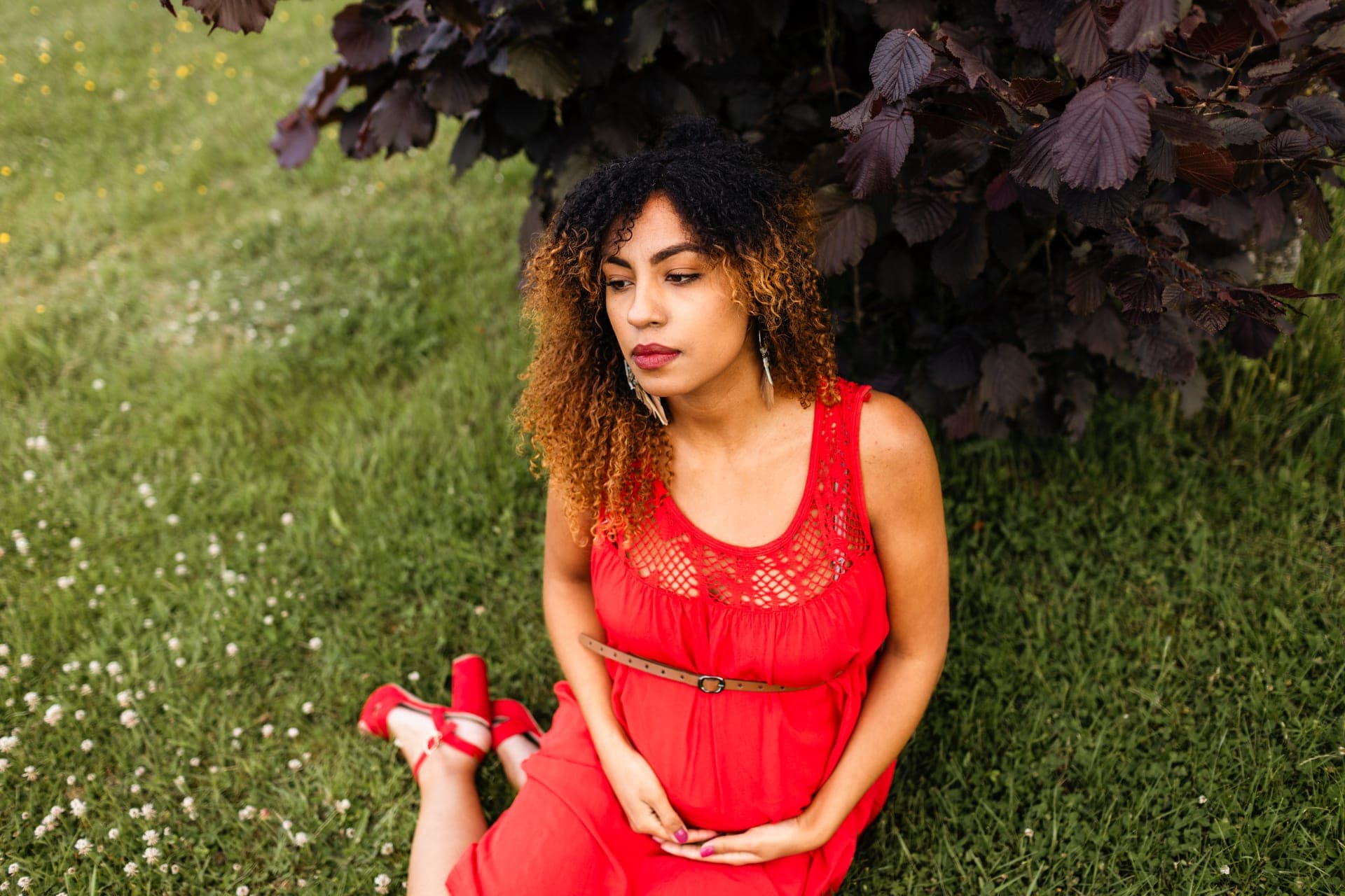 Future maman robe rouge devant arbuste pourpre — élégance grossesse