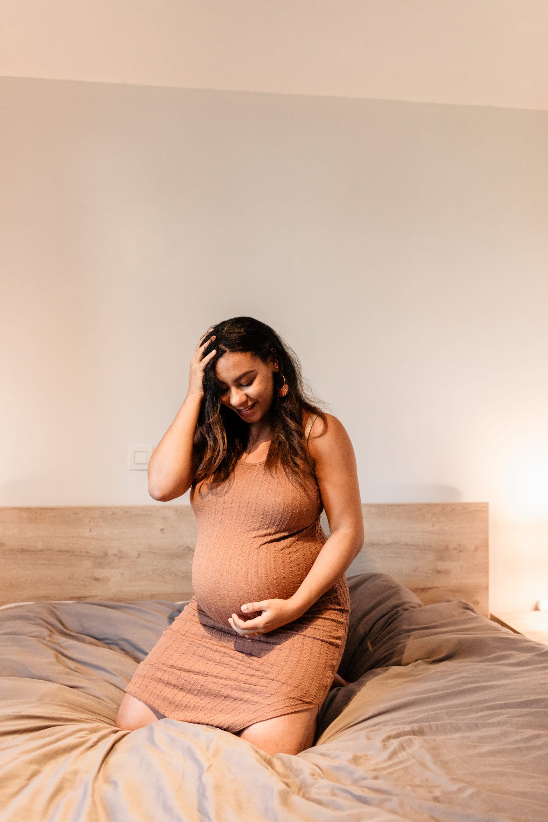 Future maman sourire paisible sur le lit robe caramel — sérénité grossesse
