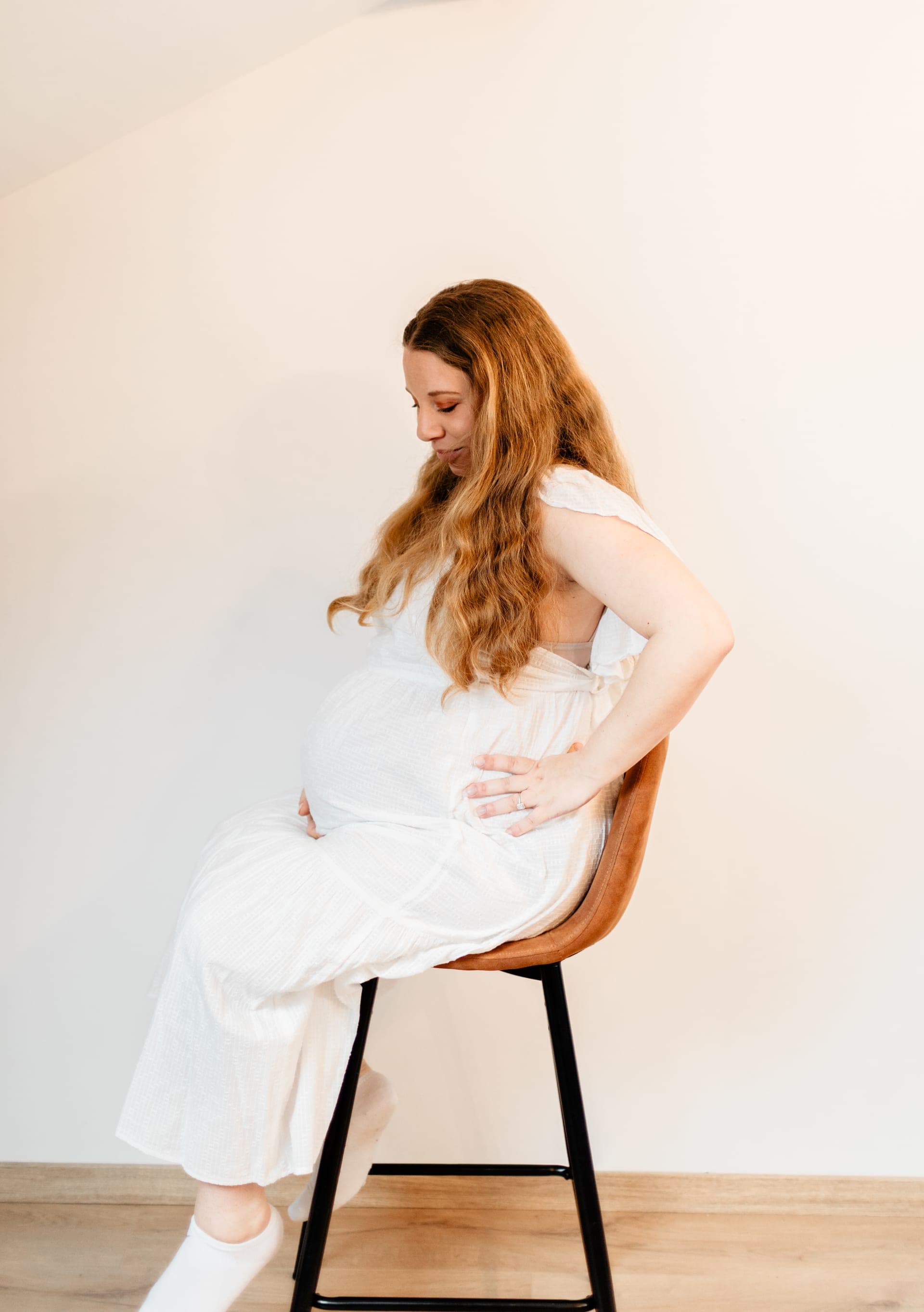 Femme enceinte rousse en robe blanche assise sur tabouret — studio grossesse Brabant Wallon