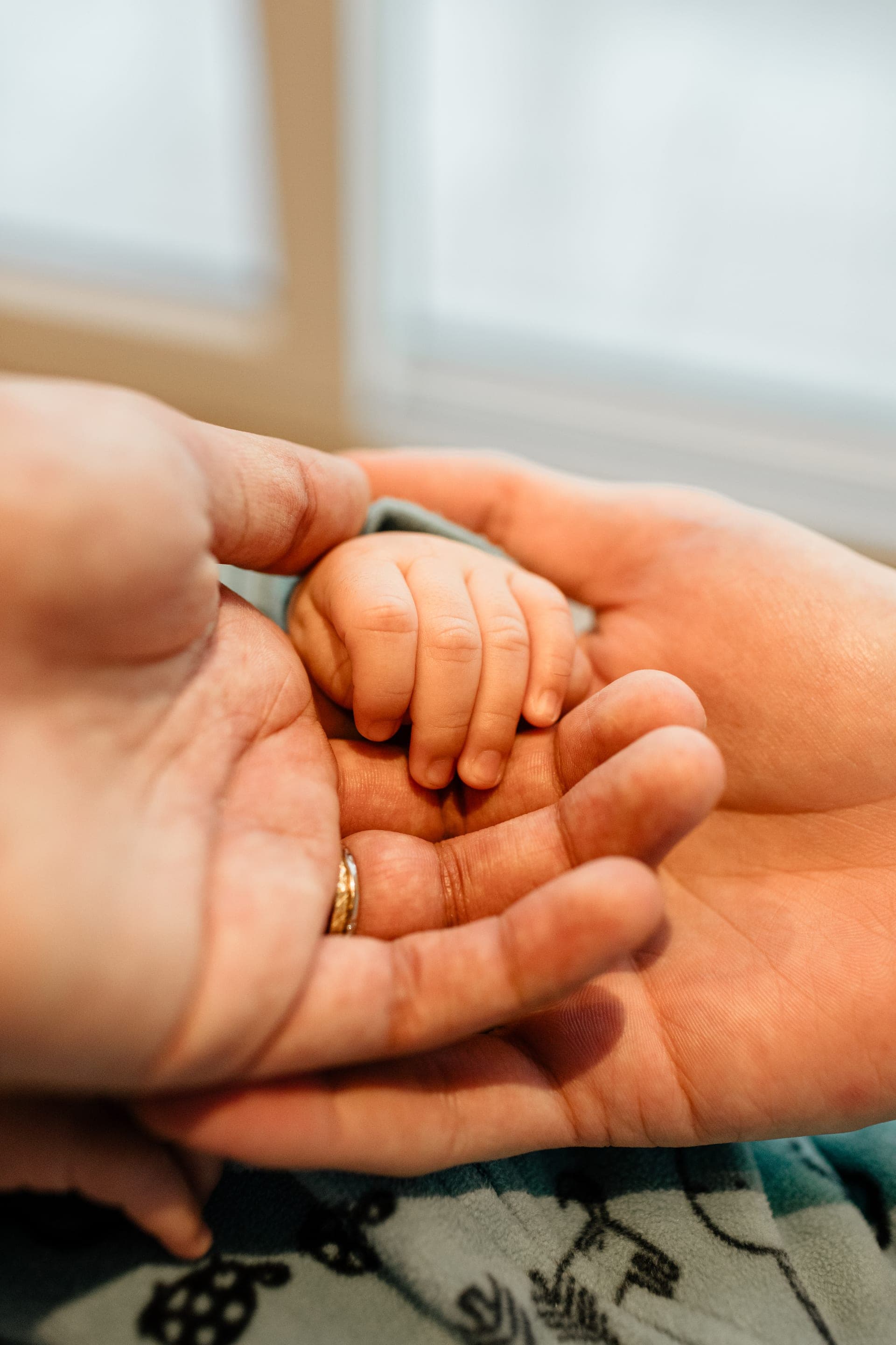 Petite main de bébé dans les mains des parents avec alliance — détail naissance émotion