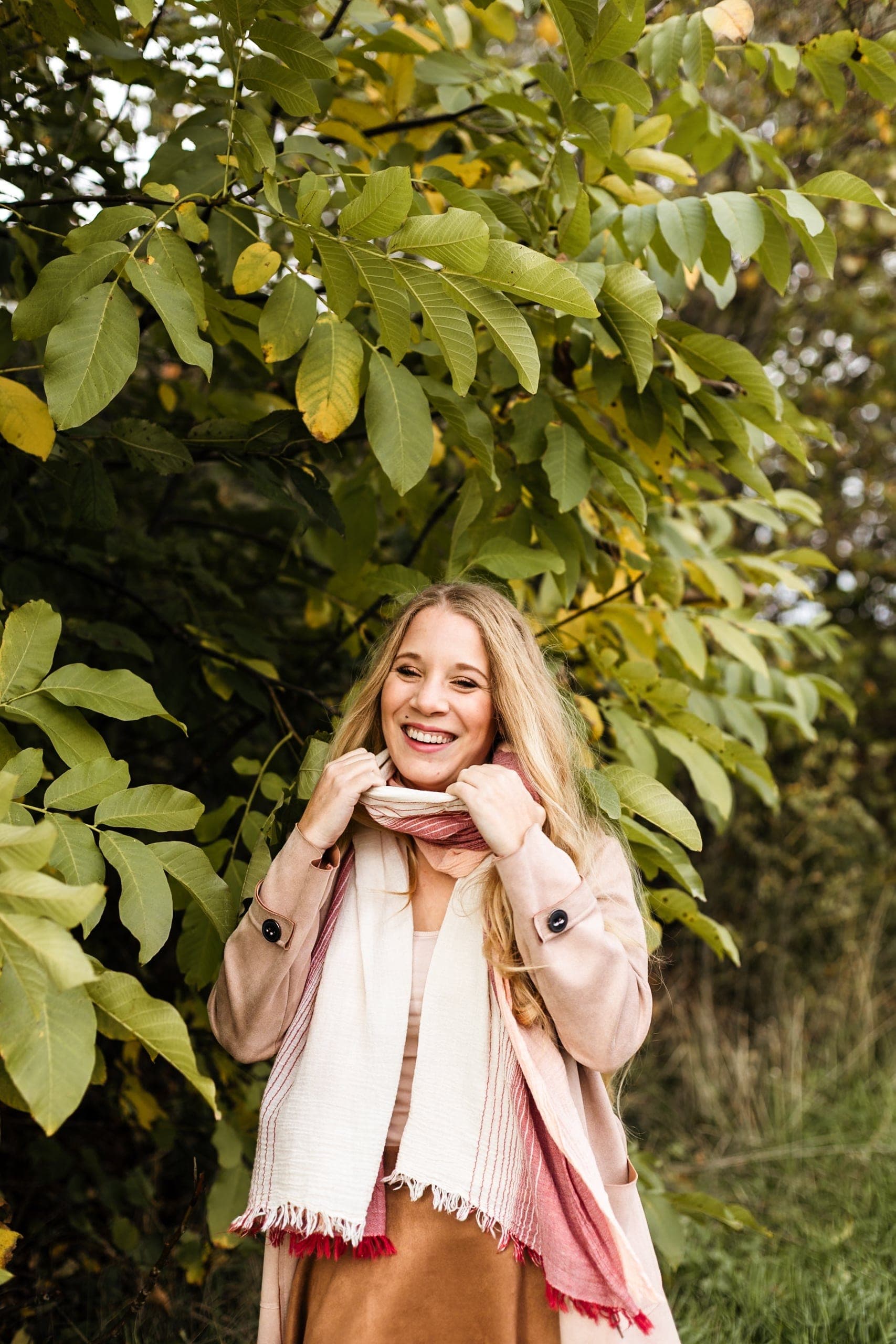 Portrait femme blonde écharpe rose éclat de rire sous feuillage d'automne — séance portrait joyeuse
