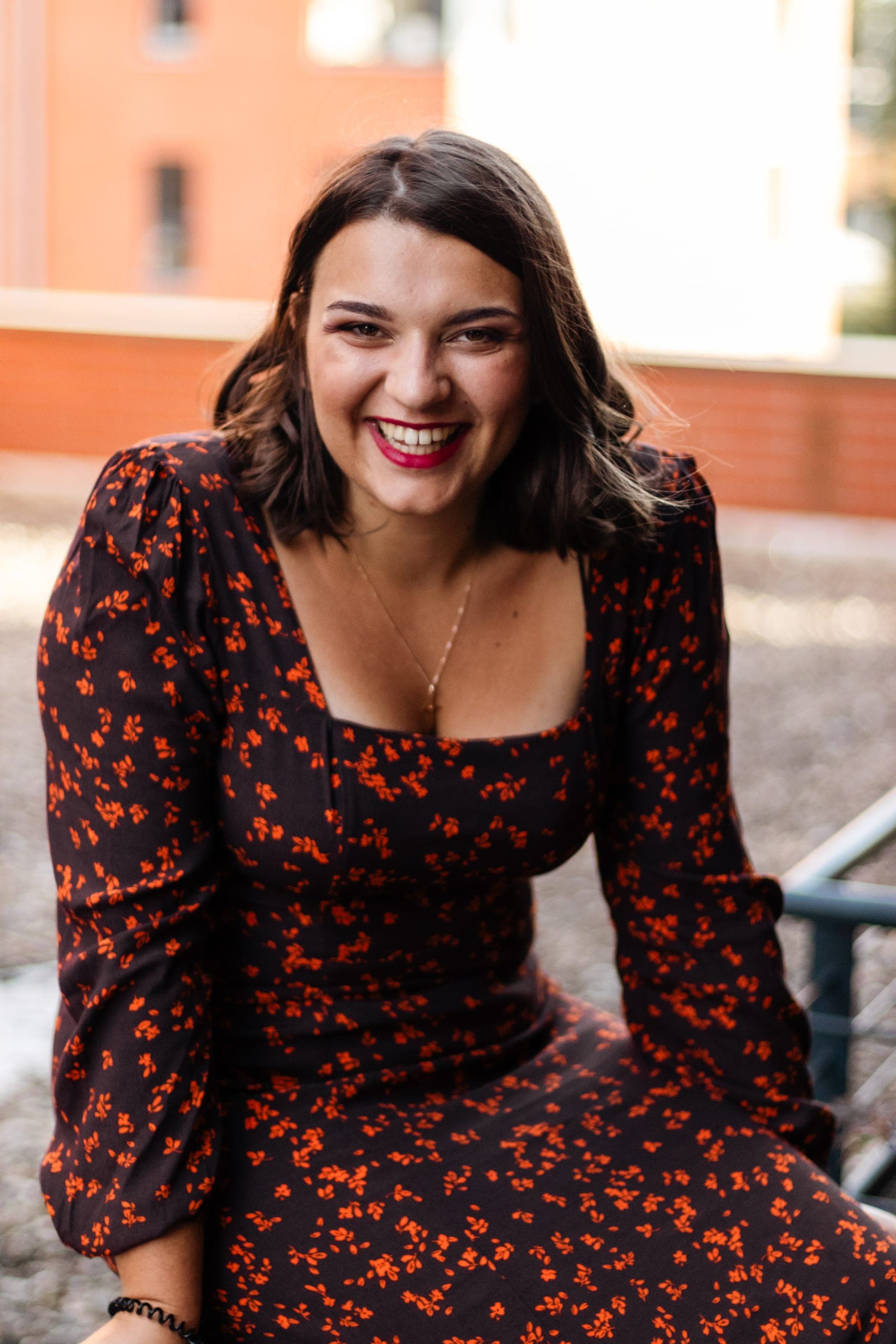 Portrait femme brune en robe noire à fleurs rouges éclat de rire en ville — séance portrait Brabant Wallon
