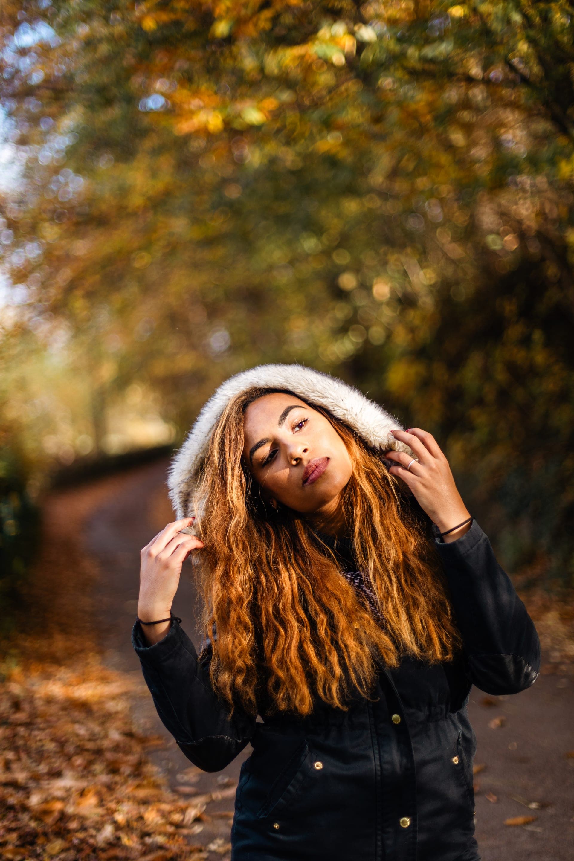 Portrait femme capuche fausse fourrure regard intense sur chemin d'automne — séance portrait