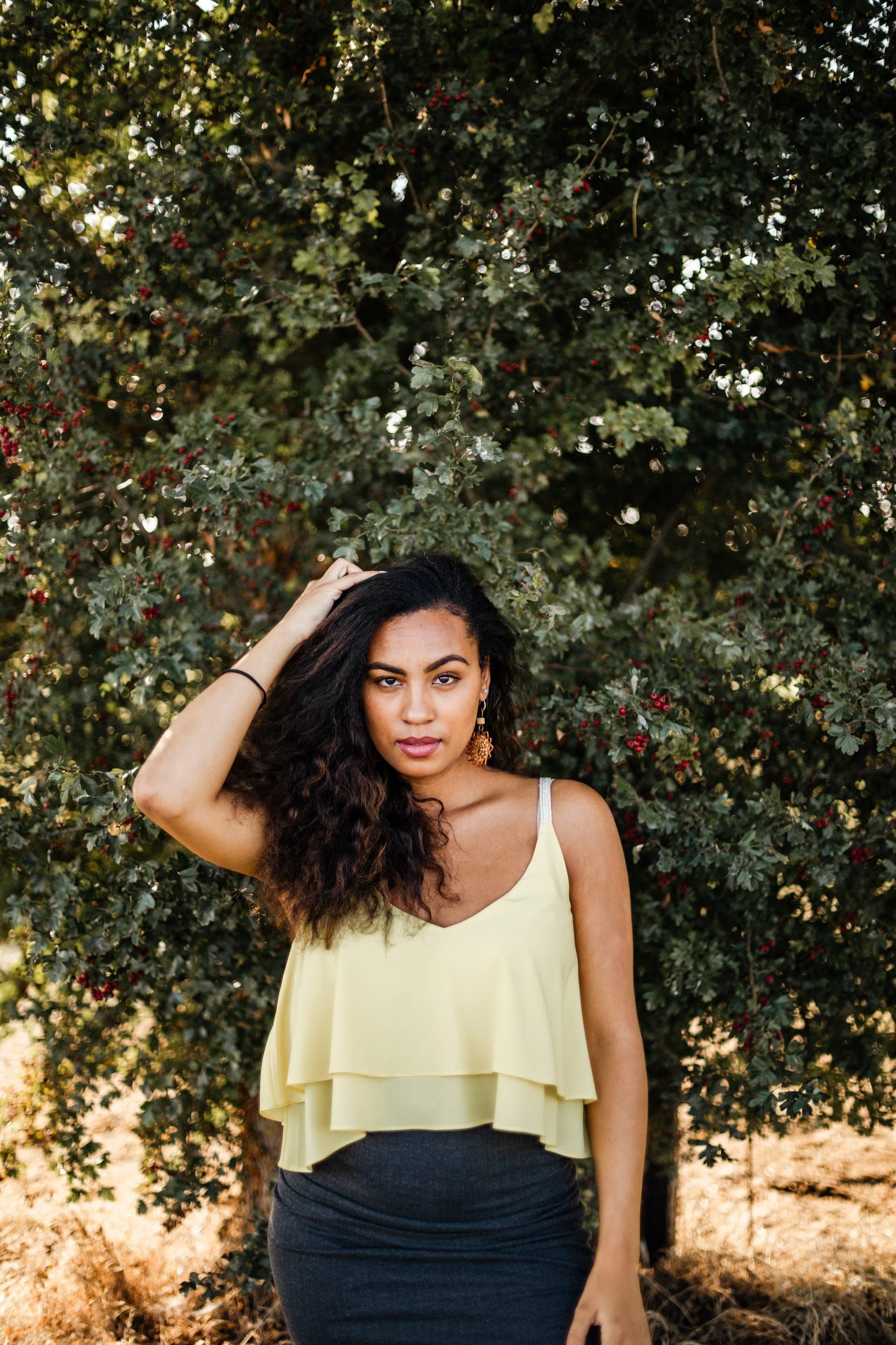Portrait femme main dans les cheveux top jaune devant feuillage vert et baies rouges — séance portrait éditorial été