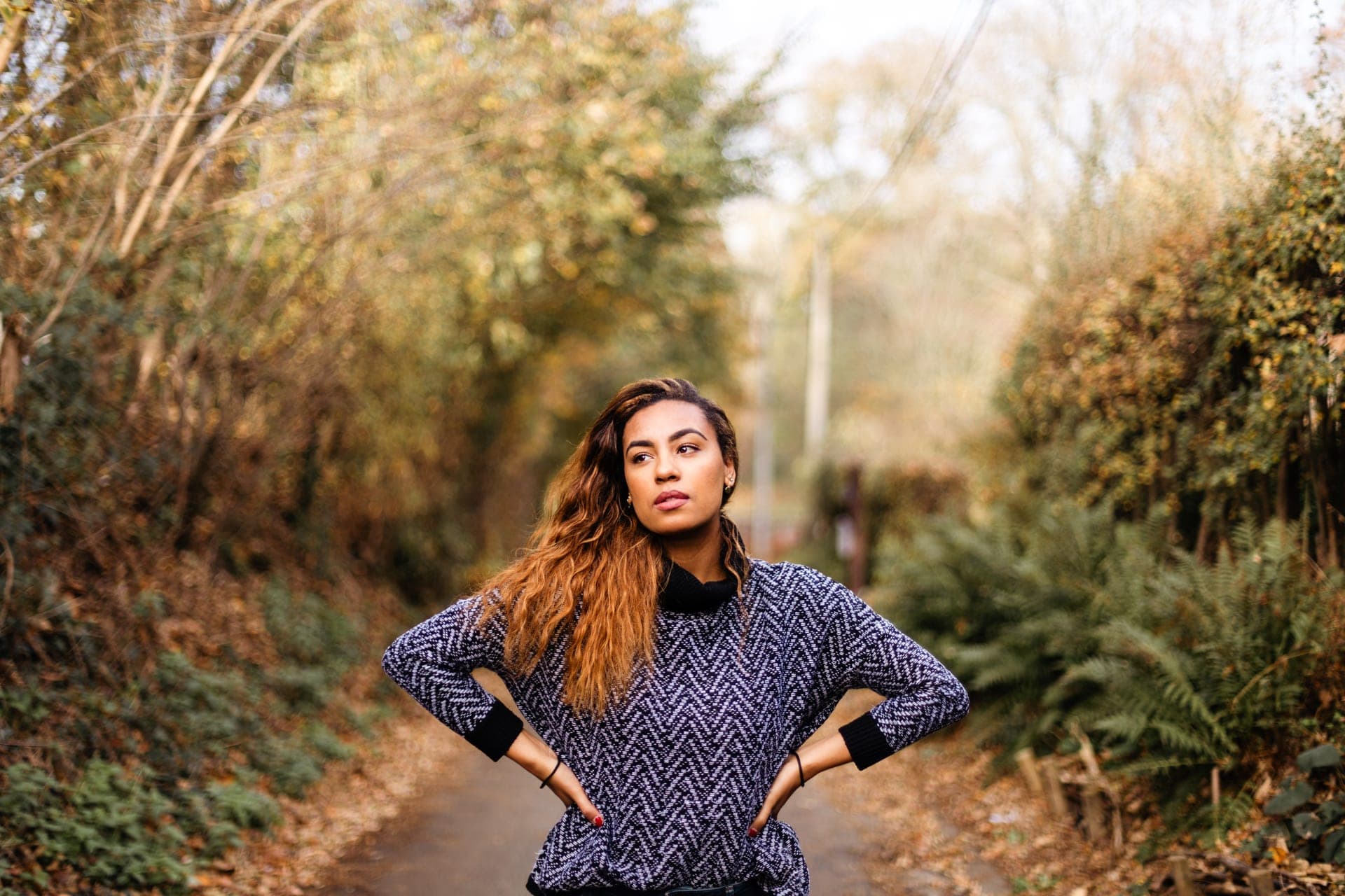 Portrait femme pull chevron bleu mains sur les hanches debout sur un chemin de forêt en automne — séance portrait Aurore Clercq Photographie Brabant Wallon