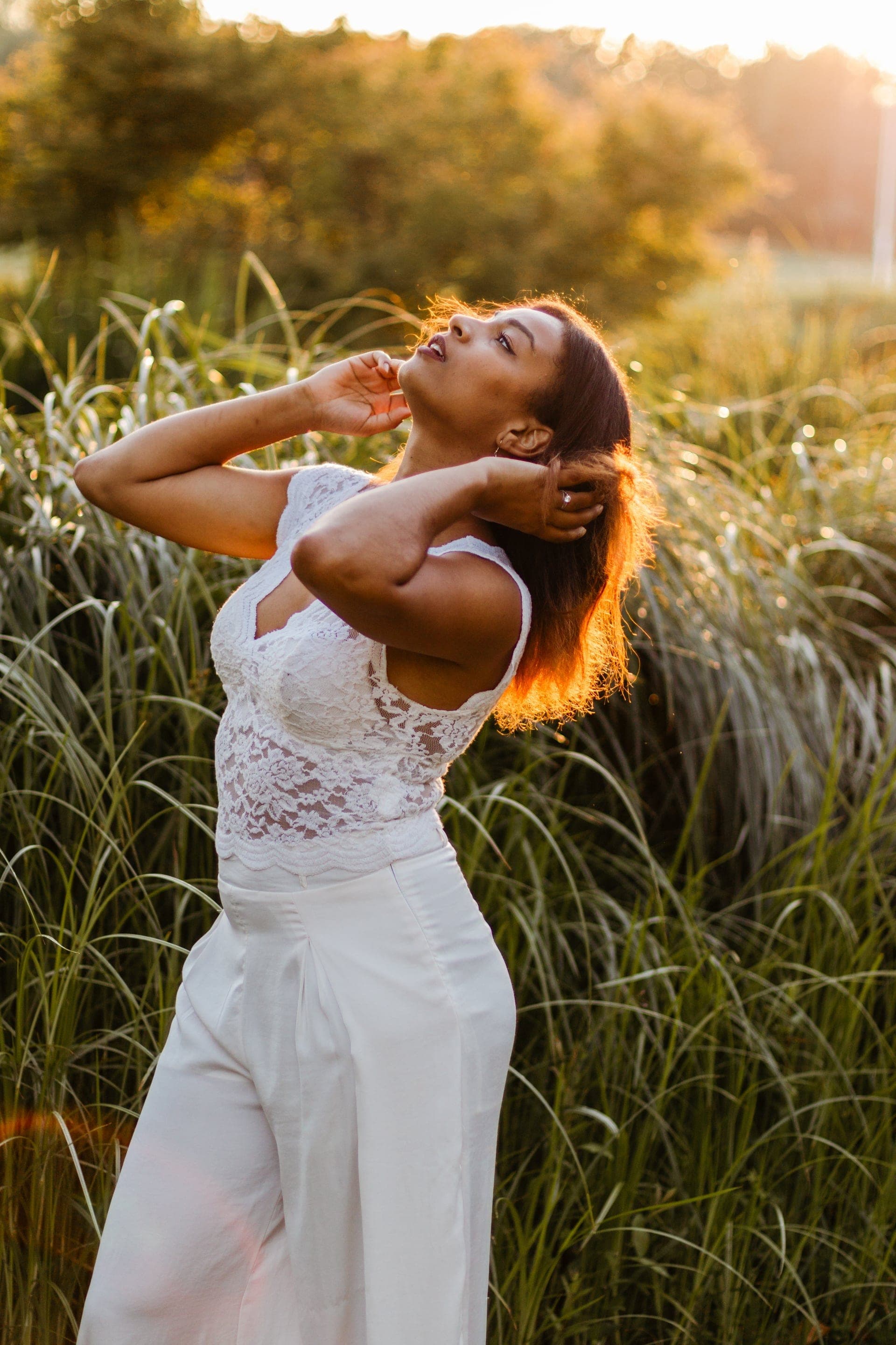Portrait femme top dentelle blanc contre-jour doré dans les herbes hautes — séance portrait golden hour