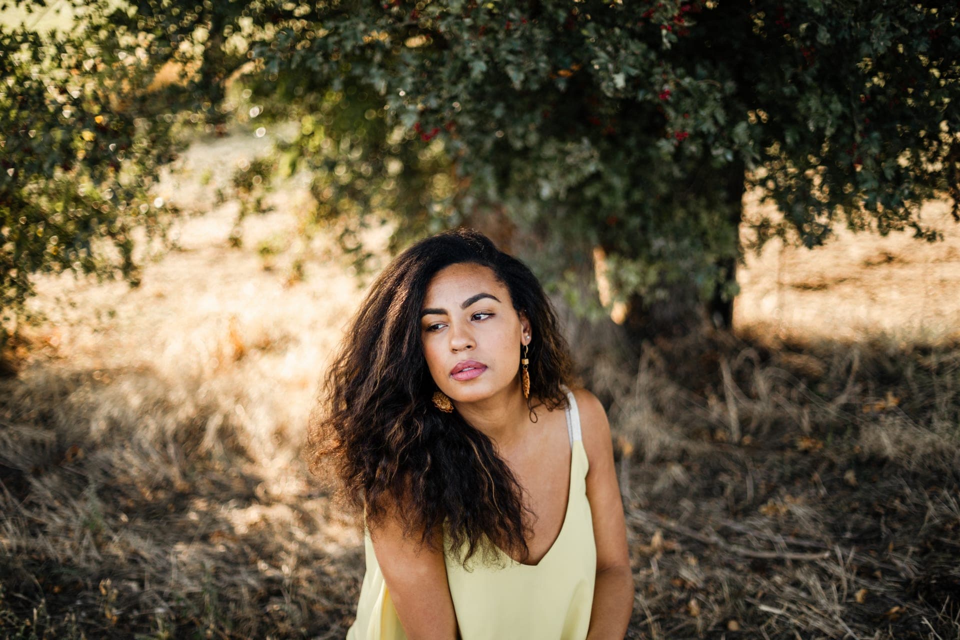 Portrait femme top jaune sous un arbre herbes dorées regard contemplatif — séance portrait lumière chaude été
