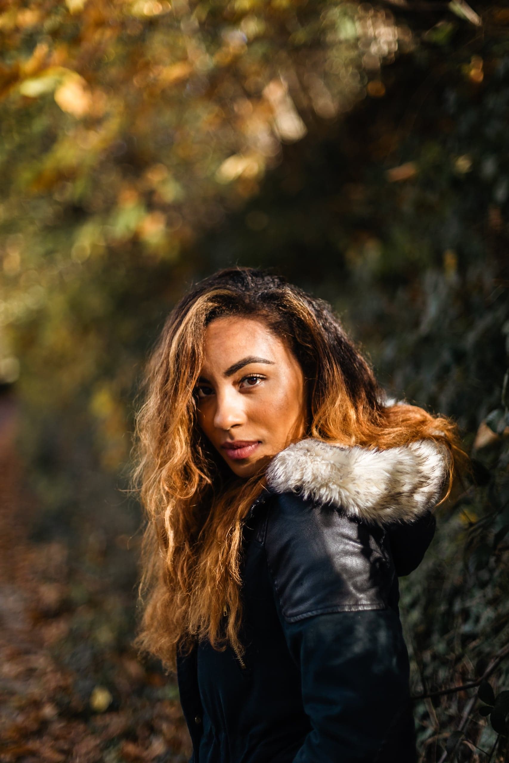 Portrait femme veste cuir col fourrure regard par-dessus l'épaule chemin d'automne — séance portrait intense