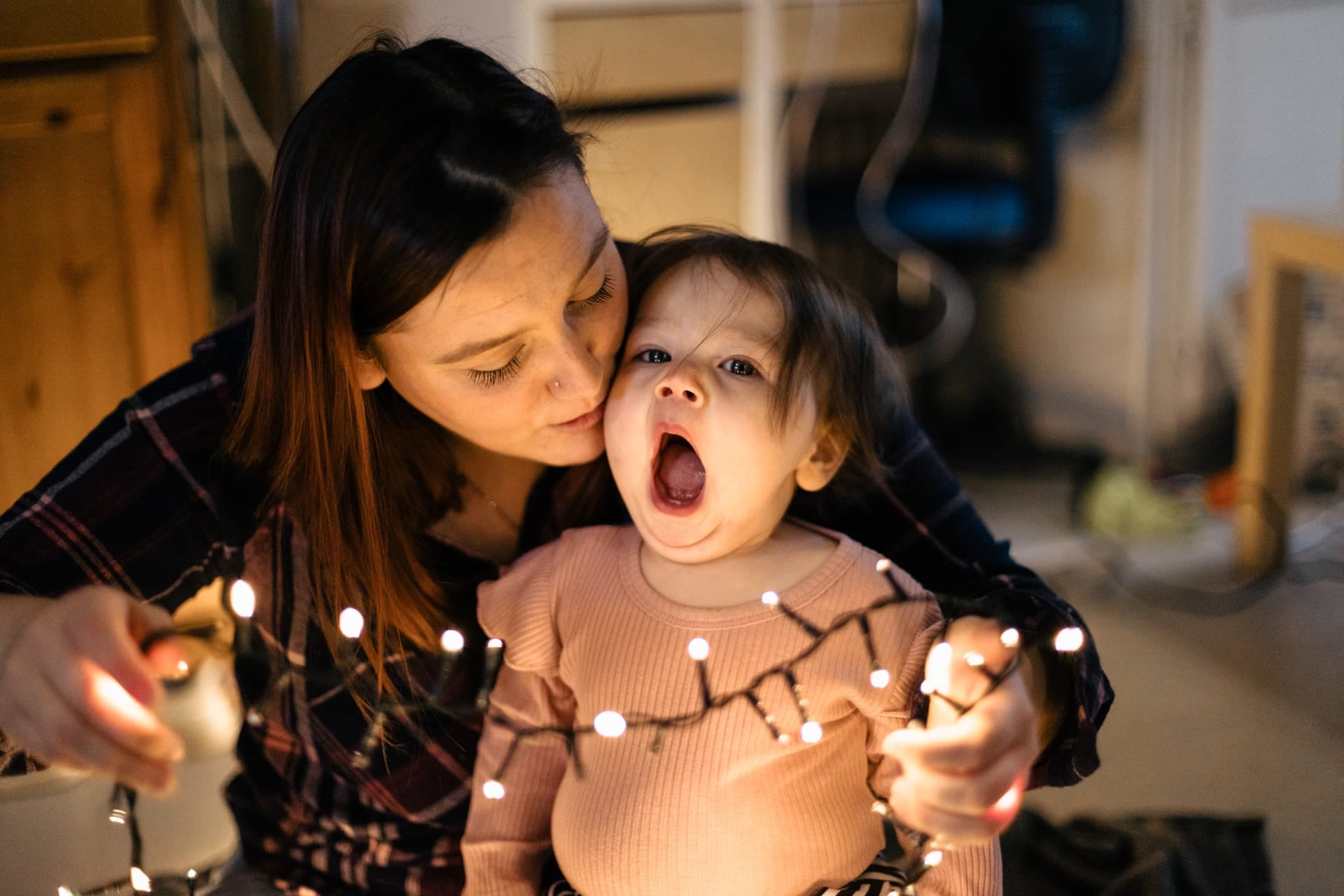 Maman et bébé avec une guirlande lumineuse fou rire — séance famille Noël intimiste Brabant Wallon et Namur