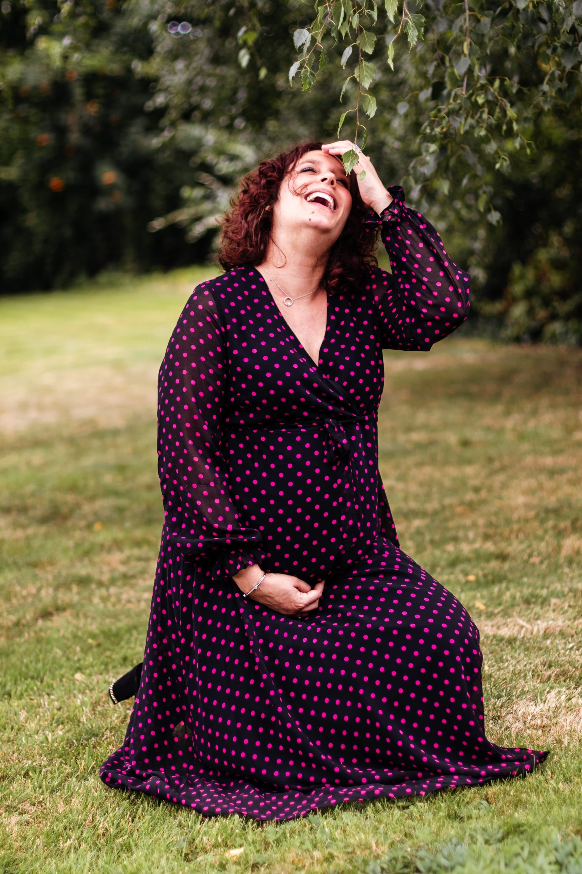 Future maman éclat de rire sous un pommier robe à pois — approche Aurore Clercq Photographie Brabant Wallon