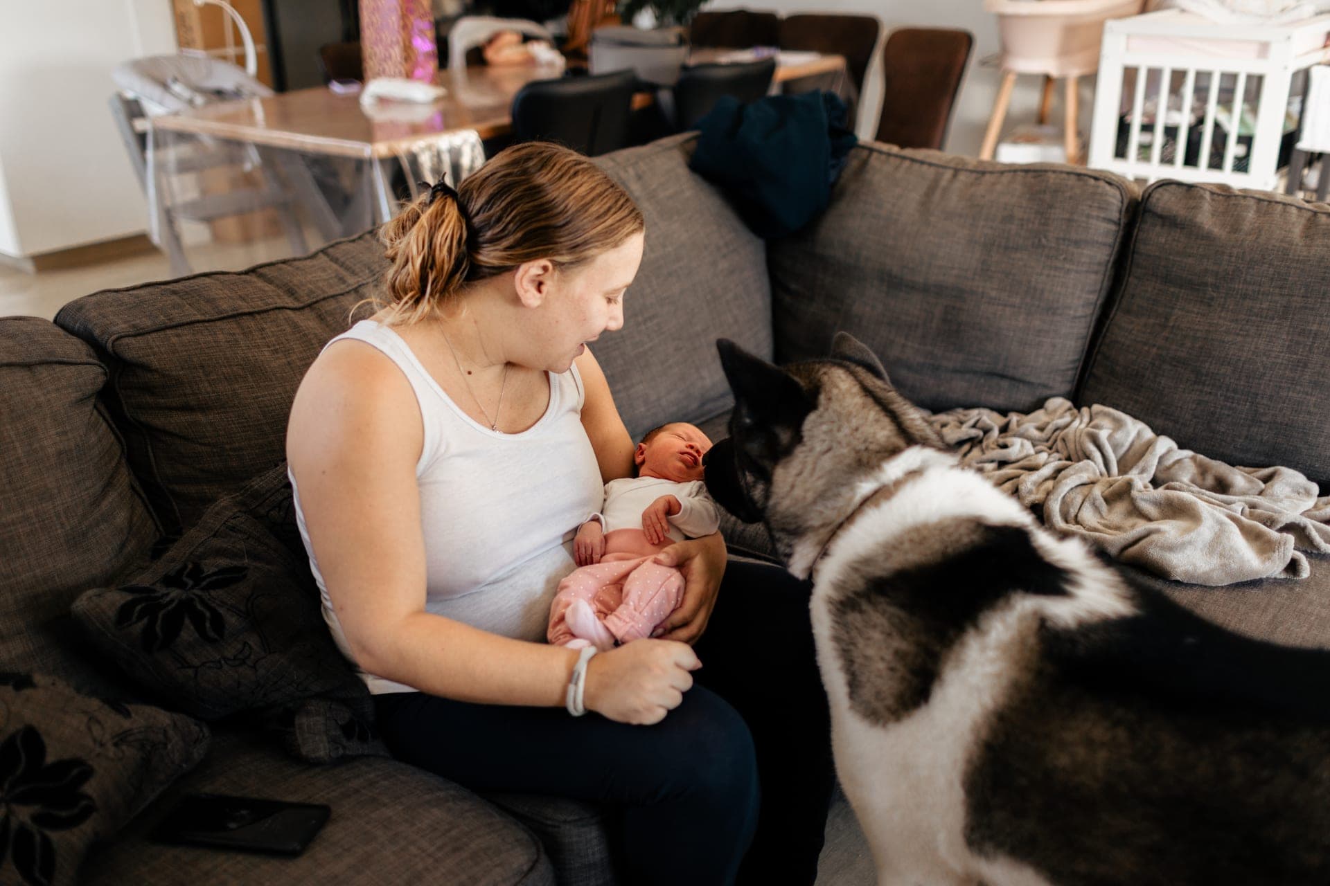 Maman avec son nouveau-né dans le salon, le chien de la famille couché à leurs côtés — séance naissance lifestyle à domicile